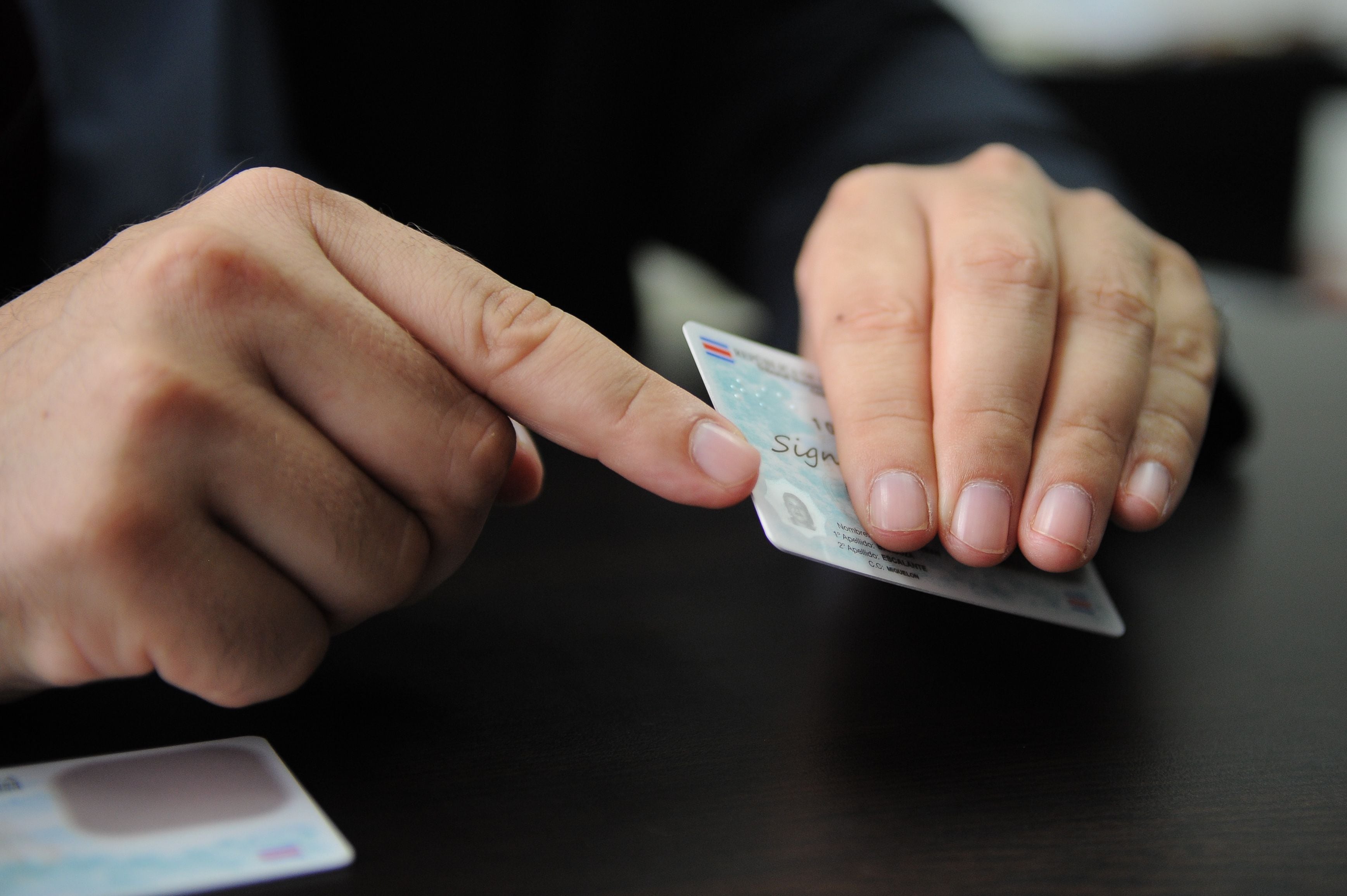 Primer plano de una persona sujetando su cédula de identidad costarricense sobre una mesa, en referencia al nuevo cobro por reposición del documento