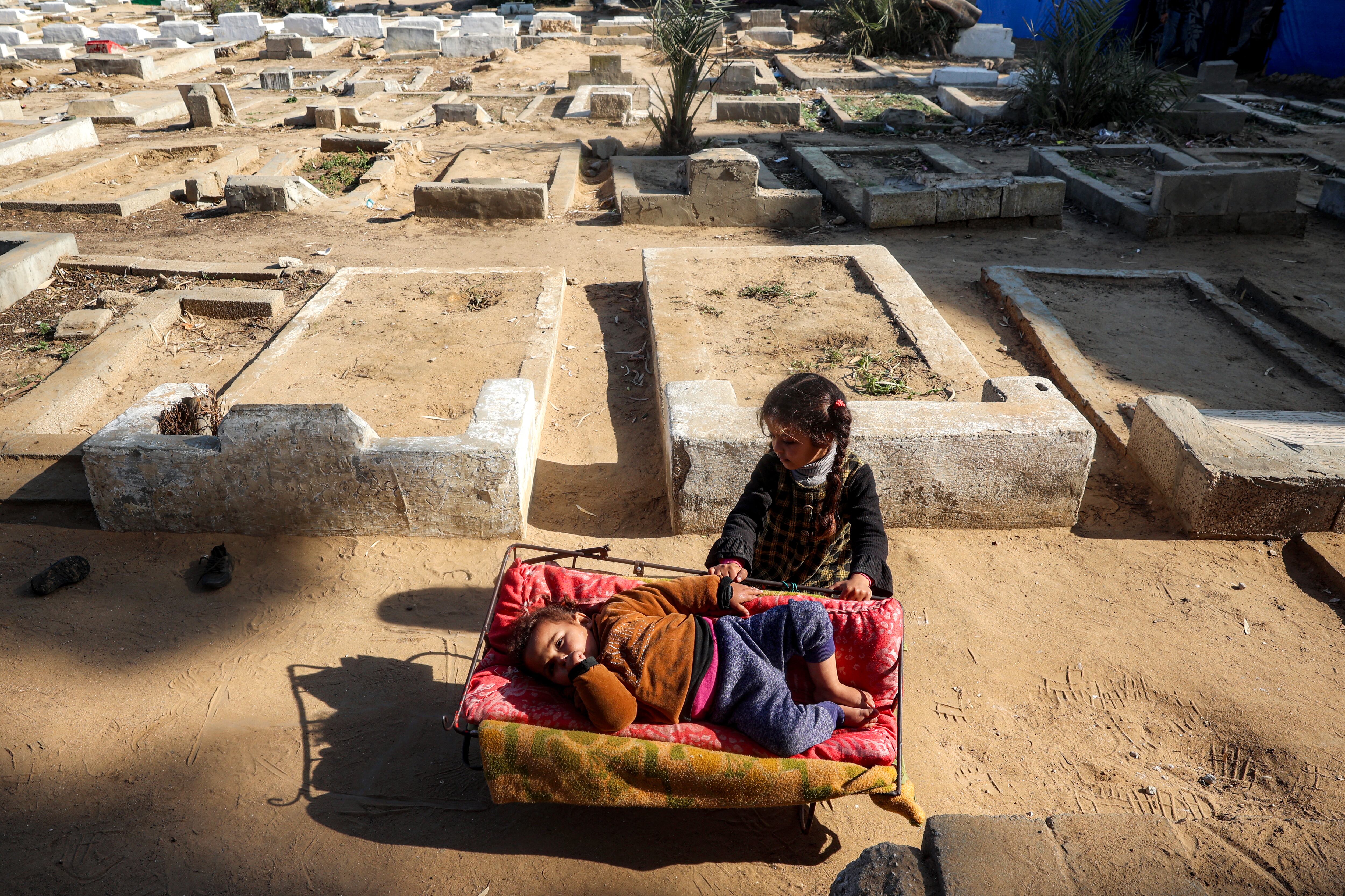 Una niña balancea una cuna de metal improvisada con un niño acostado dentro, mientras familias desplazadas por el conflicto se refugian cerca de tumbas en un cementerio en Deir el-Balah, en el centro de la Franja de Gaza, el 12 de enero de 2025, en medio de la guerra en el territorio palestino entre Israel y Hamás.
