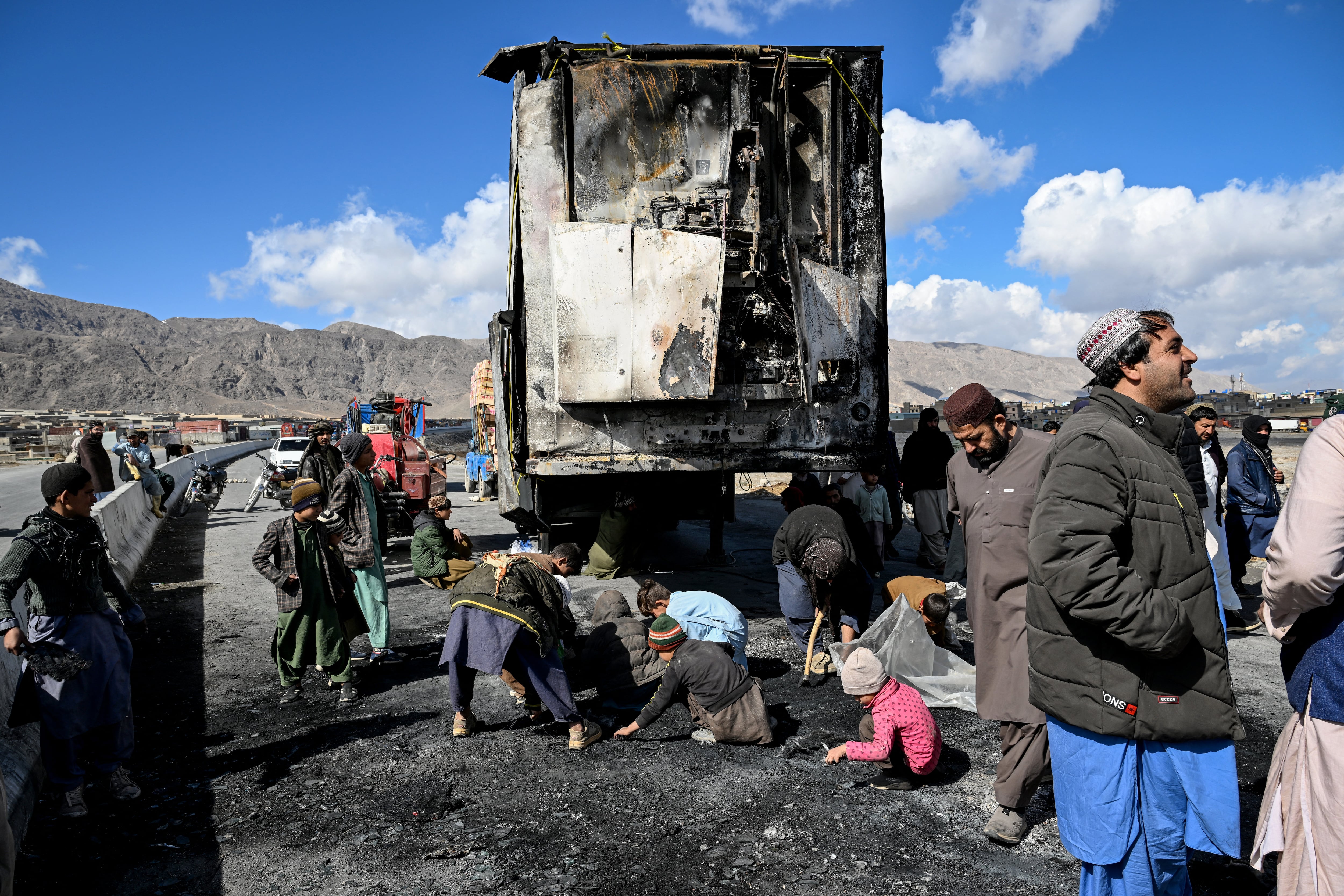 Varias personas se agrupan mientras otras recogen objetos reciclables junto a un vehículo calcinado en una carretera a las afueras de Quetta, el 1 de febrero de 2026, un día después de un ataque perpetrado por separatistas baluchis.