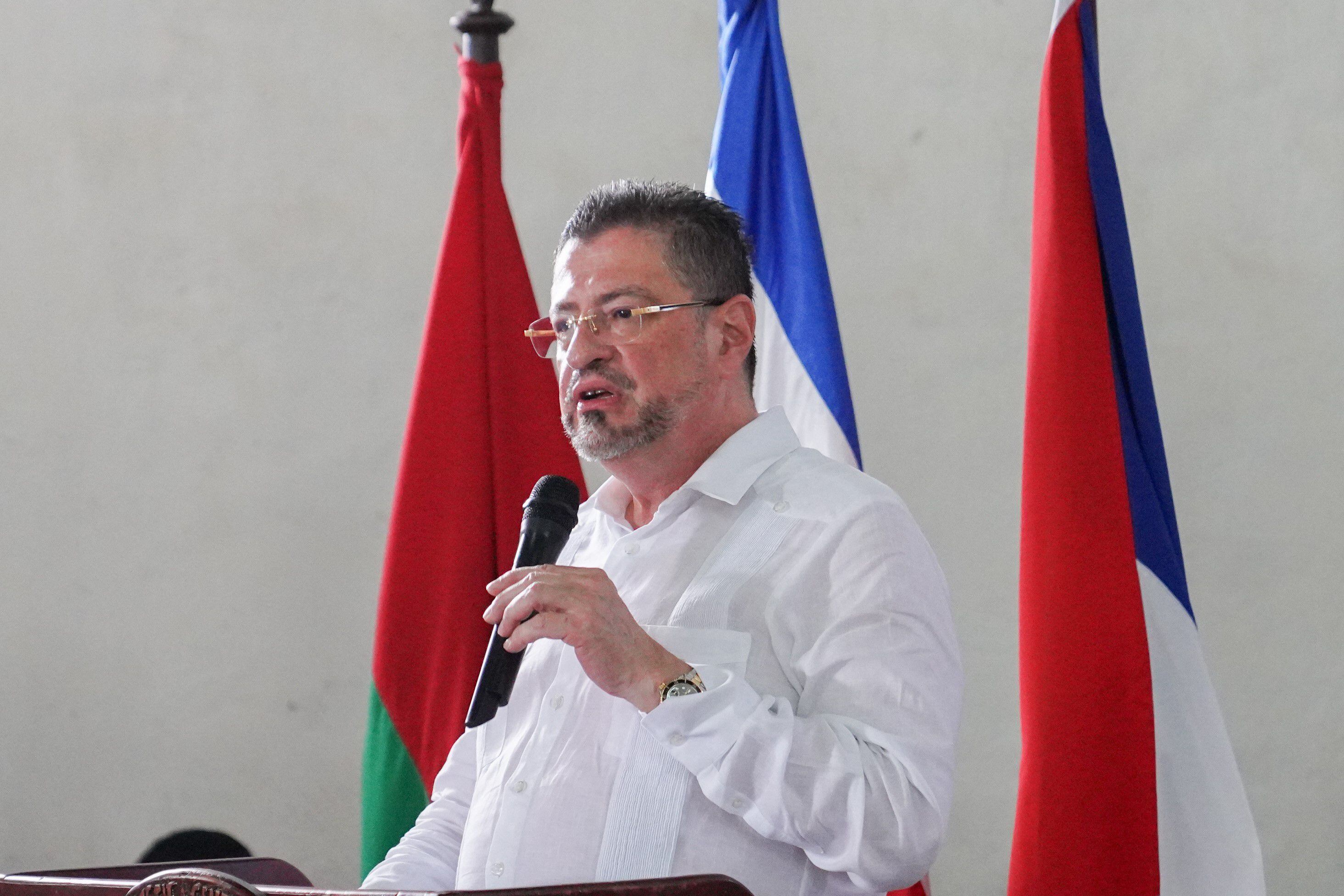 El presidente de Costa Rica, Rodrigo Chaves, vestido con camisa blanca, habla frente a un micrófono con banderas de fondo.