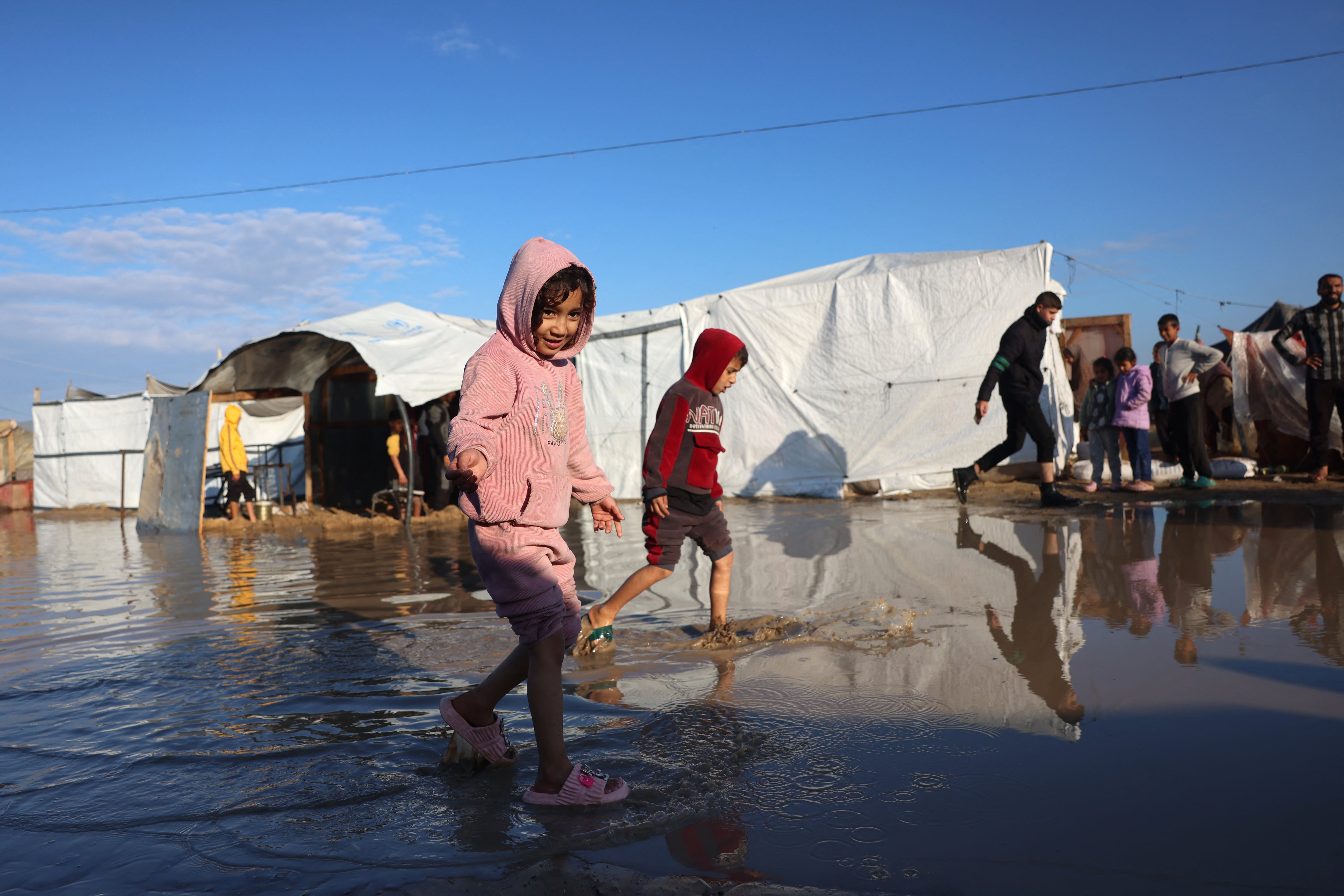 Niños palestinos desplazados caminan sobre charcos de agua frente a tiendas de campaña en un campo de refugiados en Gaza, tras fuertes lluvias y bajas temperaturas que afectan a la región.