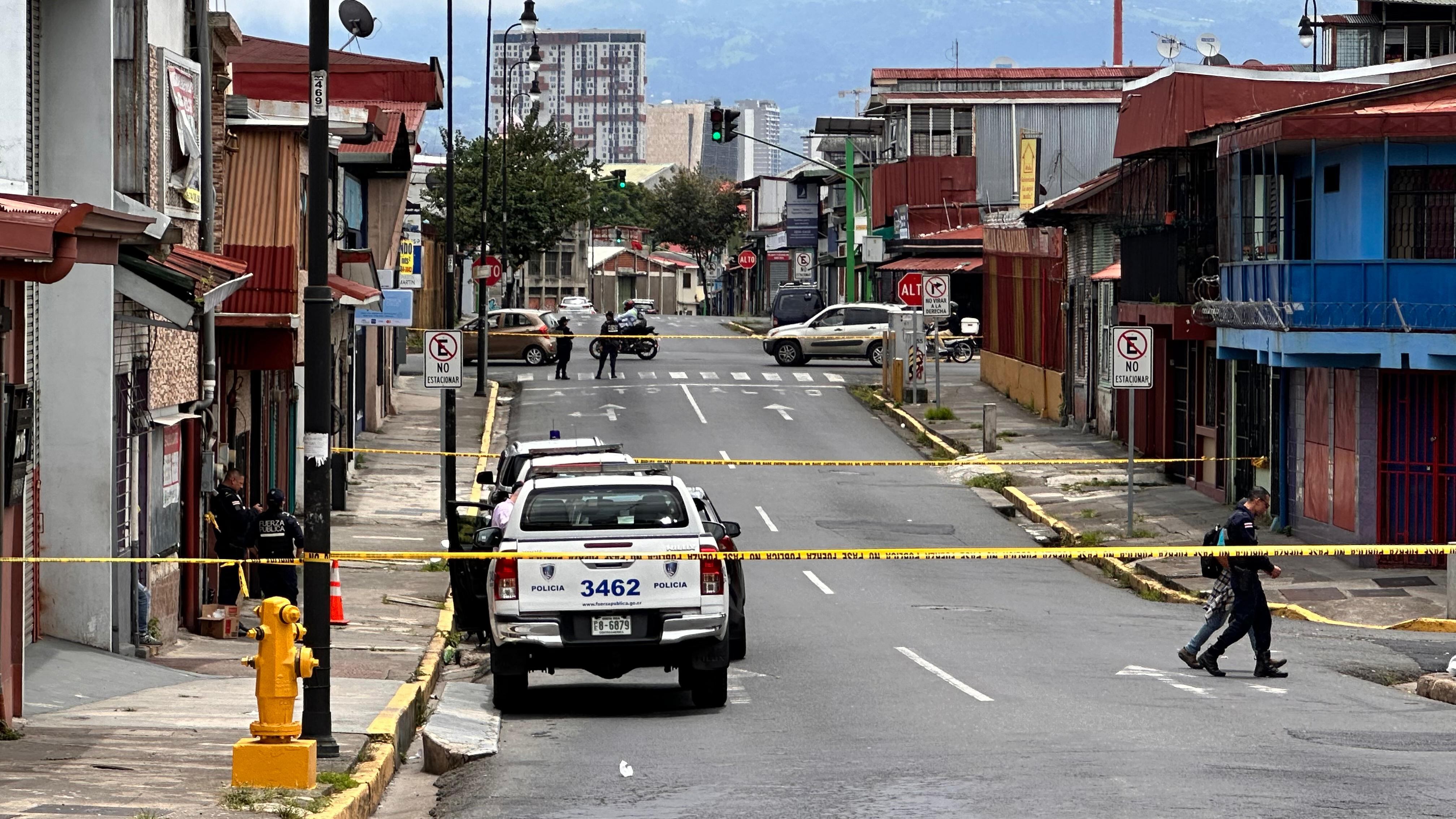 Calle acordonada en San José con patrullas policiales y cinta amarilla de seguridad, agentes de la Fuerza Pública resguardando la zona tras un incidente relacionado con la violencia en la capital.