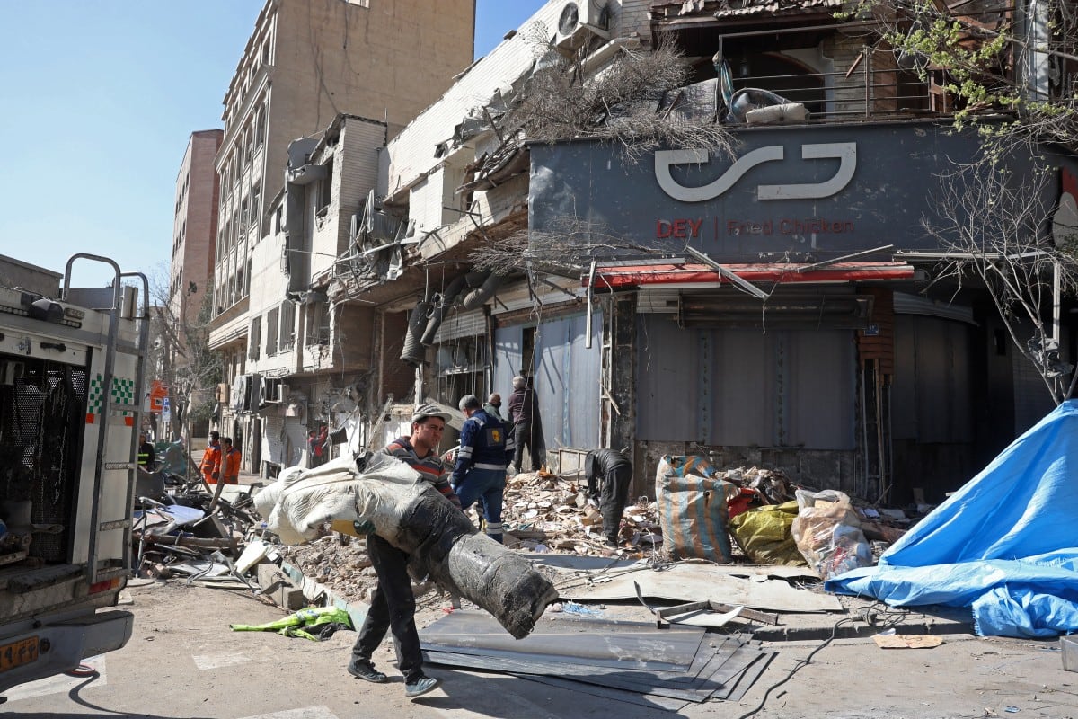 Una columna de humo se eleva mientras personas inspeccionan los escombros de un edificio dañado tras los ataques aéreos en el centro de Teherán el 4 de marzo de 2026.