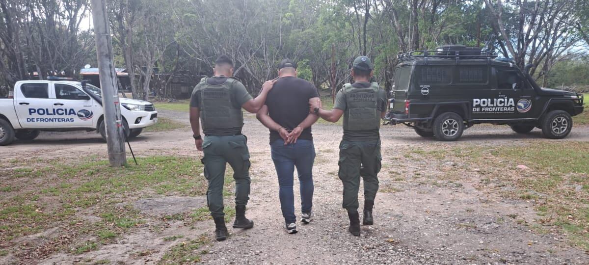 Hombre con esposas camina acompañado por dos policías hacia una patrulla.