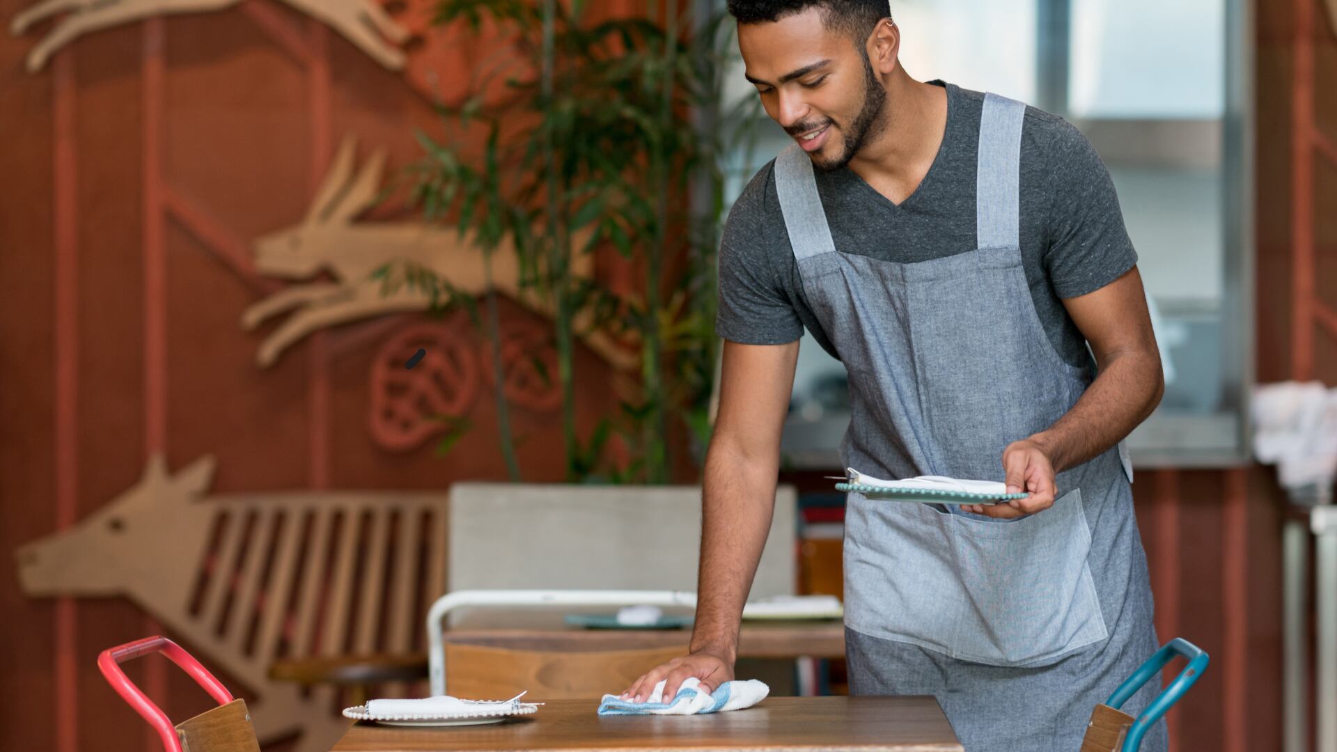 Empleado de restaurante limpia una mesa mientras sostiene platos, en el contexto de los feriados de pago obligatorio en abril de 2025 en Costa Rica.