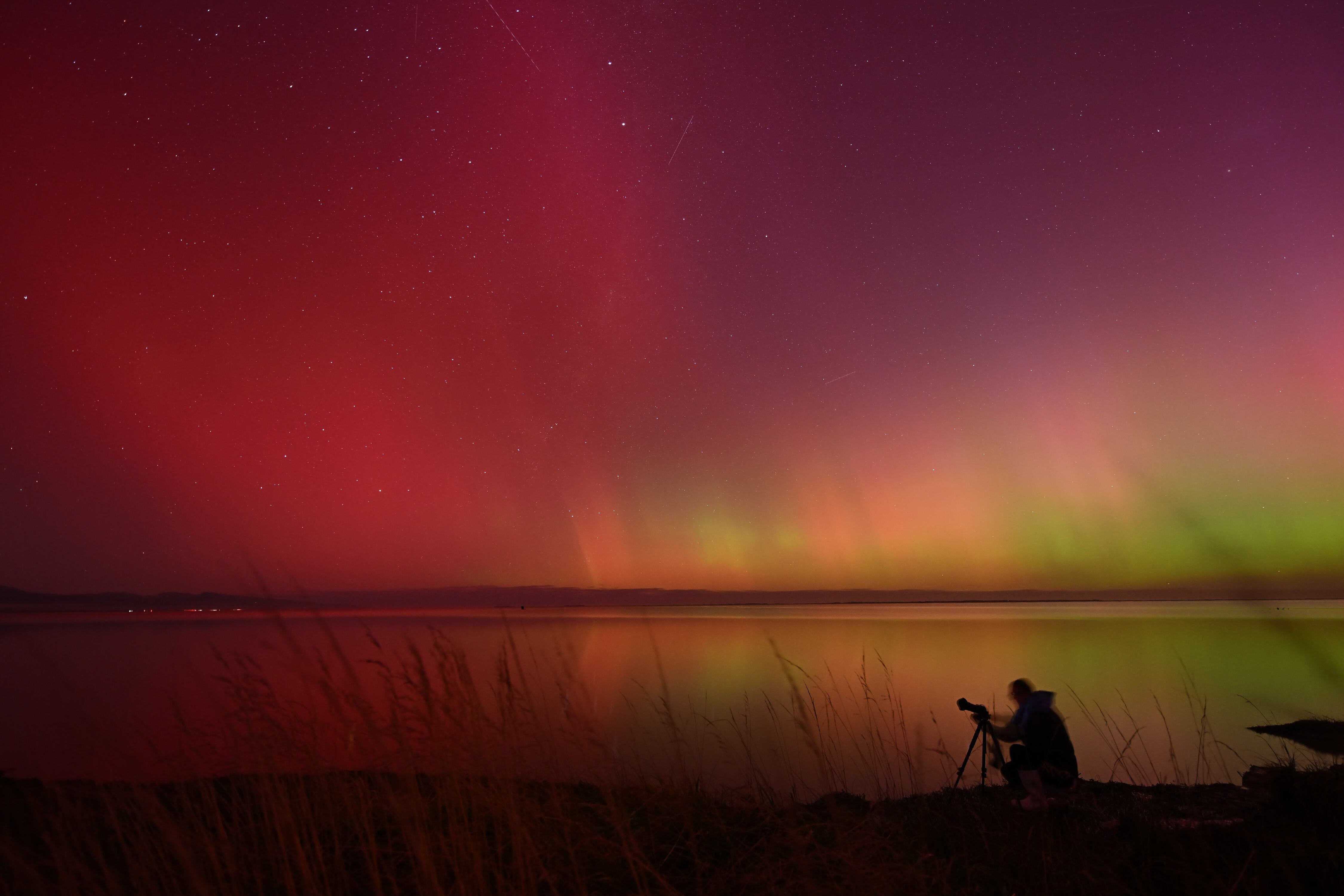 Un fotógrafo captura imágenes de la Aurora Austral, también conocida como Luces del Sur, que resplandece en el horizonte sobre las aguas del lago Ellesmere en las afueras de Christchurch el 11 de mayo de 2024. Foto: AFP