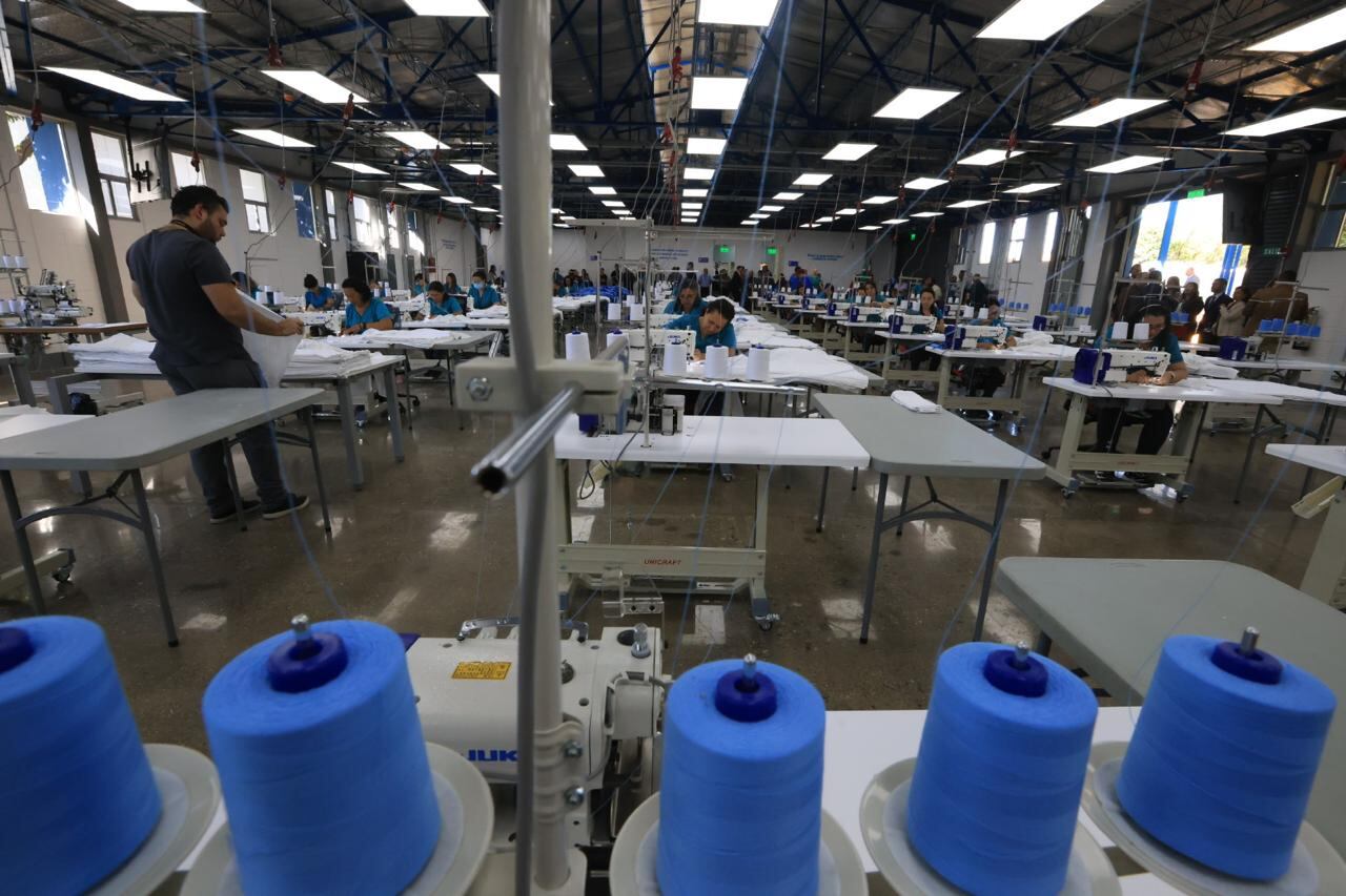 Salón enorme de una fábrica de ropa con grandes hilos azules para ropa hospitalaria. Techo con grandes luces artificiales blancas.