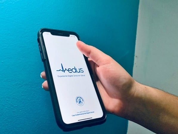 Mano sostiene un teléfono celular con pantalla blanca sobre la cual se lee la palabra EDUS.