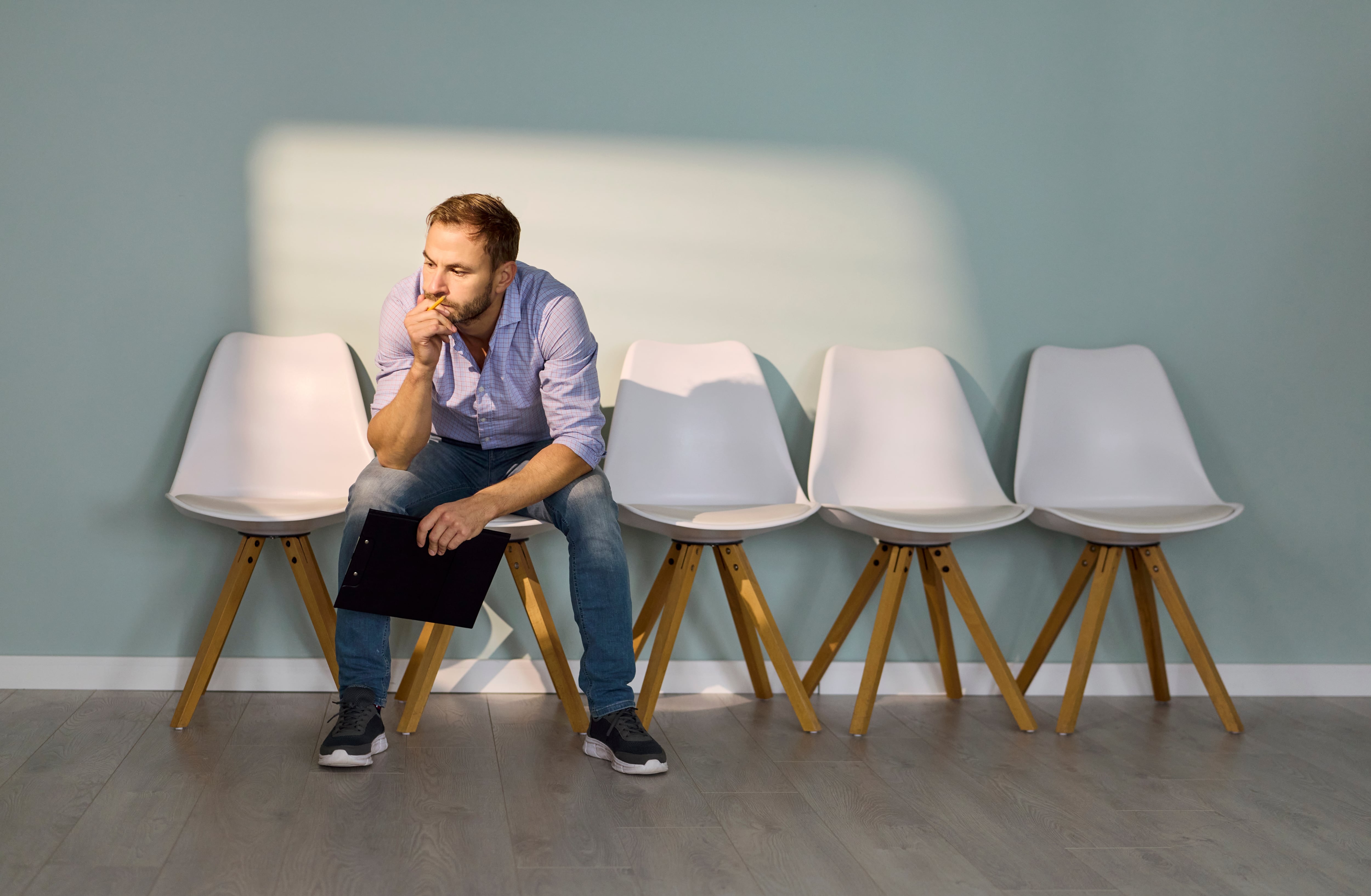 Un empleado esperando una entrevista en el pasillo de la oficina. Un hombre busca trabajo. Candidato sentado en una silla con un currículum, ensayando respuestas a medida que crece la ansiedad. Concepto de contratación, desempleo