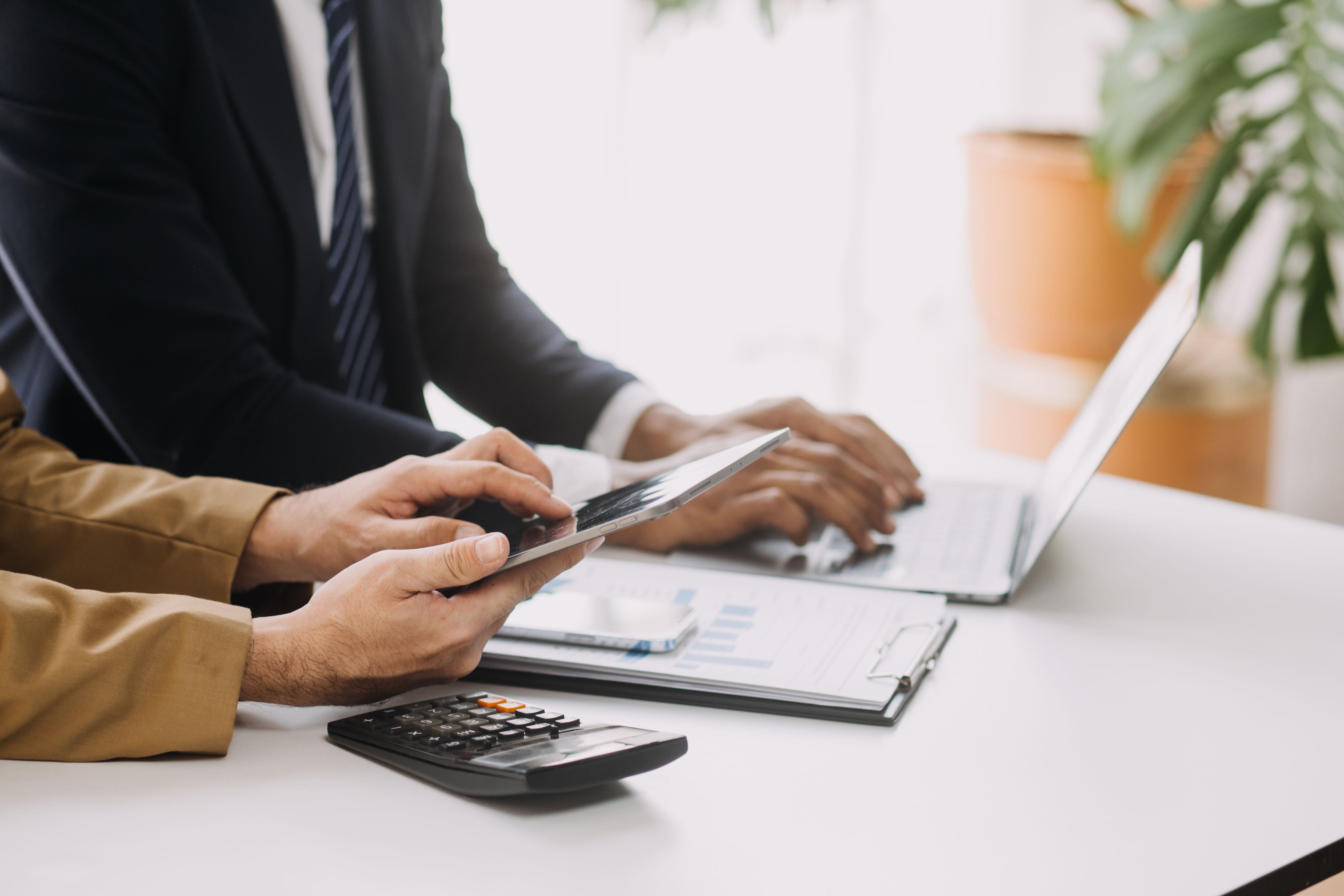 Manos de dos personas frente a un escritorio, una sostiene una calculadora y otra escribe en una computadora