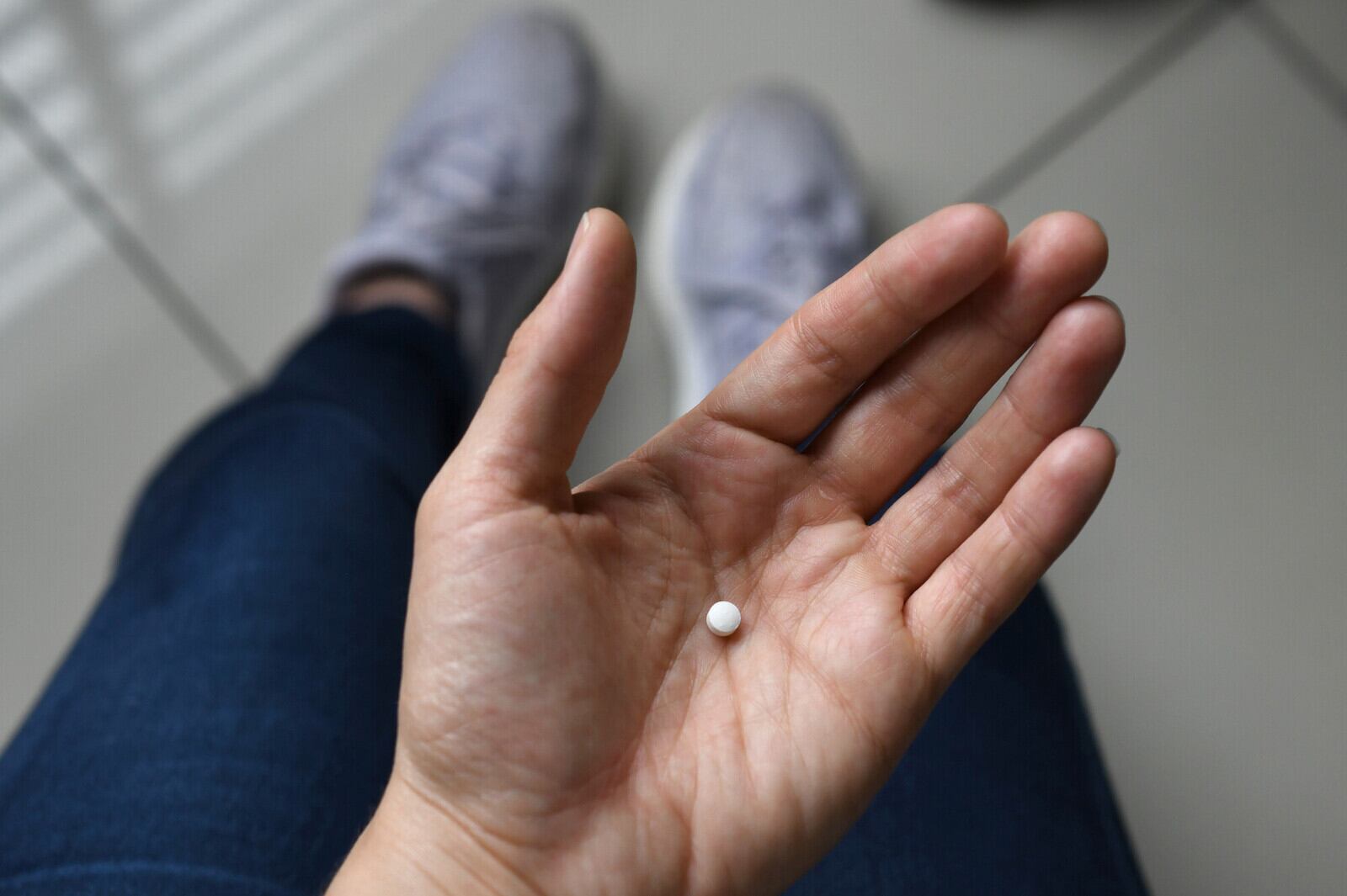 Una mano sostiene una pequeña píldora de color blanco.