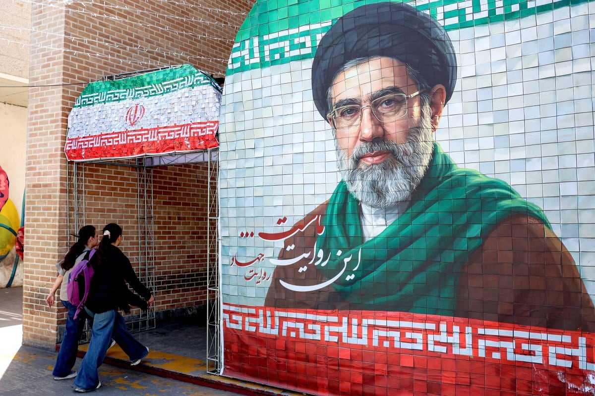 Mujeres pasan junto a una pancarta que representa al actual líder supremo de Irán, el ayatolá Mojtaba Khamenei, a lo largo de una calle de Teherán.