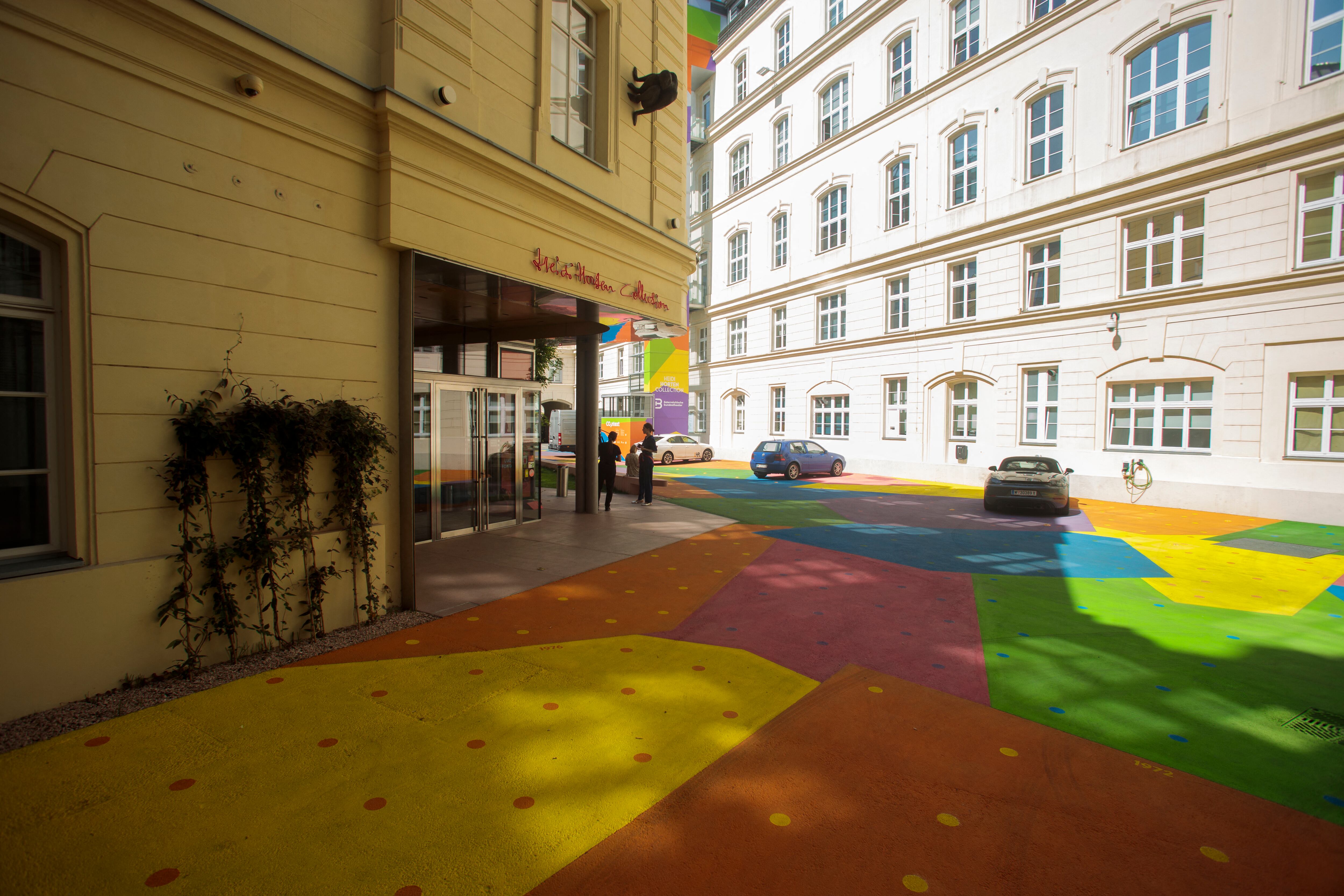 A view from above shows people and cars on the colourfully painted courtyard of the 'Heidi Horten museum' is pictured in Vienna, Austria, on August 13, 2025. To fight extreme heat attributable to climate change, an artist collective has covered the asphalt with reflective paints to lower the temperature, as part of an innovative project in Europe combining art, science, and urban development. (Photo by Alex HALADA / AFP)