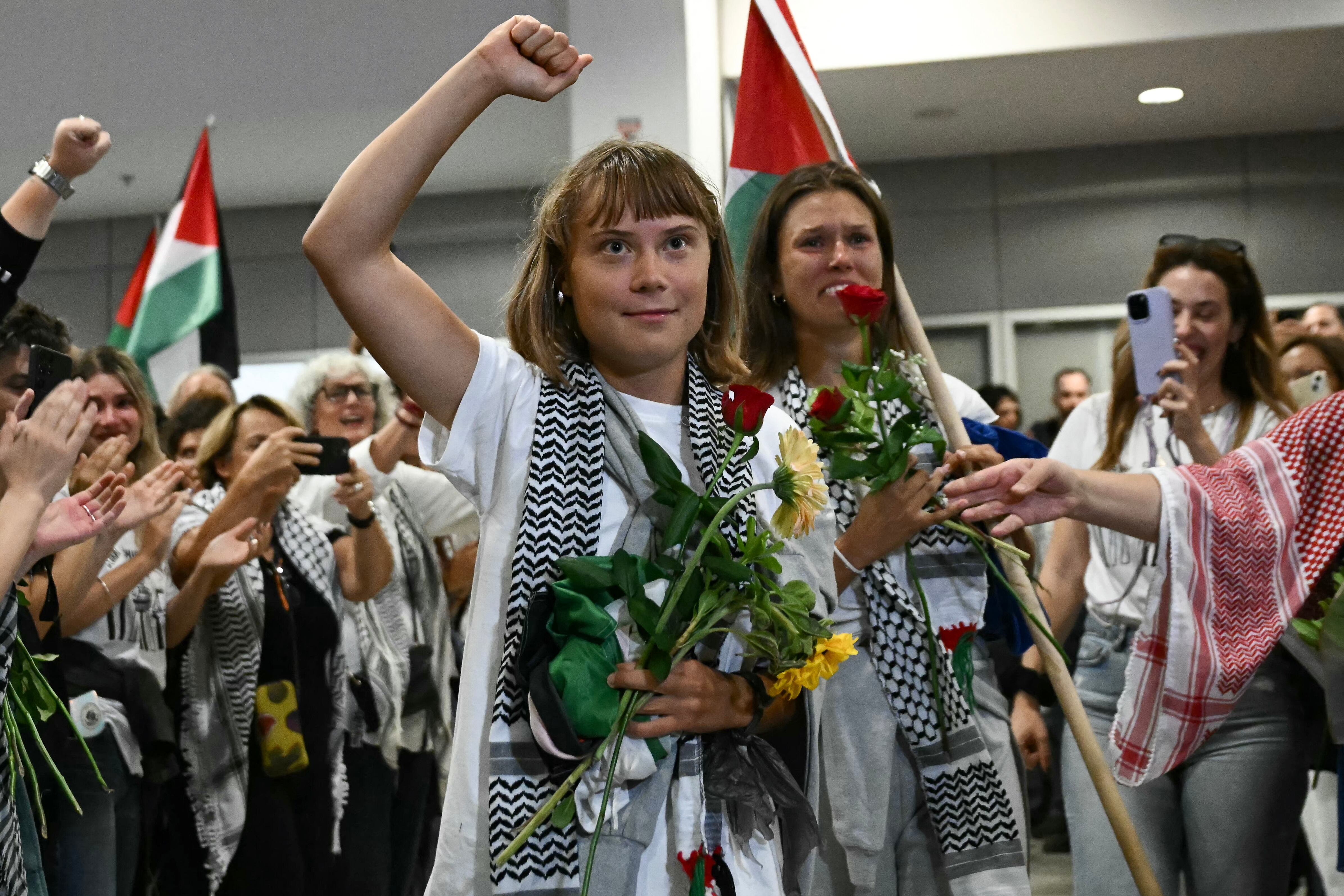 La activista climática sueca Greta Thunberg levanta el puño al llegar junto a activistas que navegaban a bordo de los barcos de la flotilla de ayuda a Gaza antes de ser detenidos por las fuerzas israelíes, recibidos por una multitud de simpatizantes, en la zona de llegadas del Aeropuerto Internacional de Atenas el 6 de octubre de 2025.