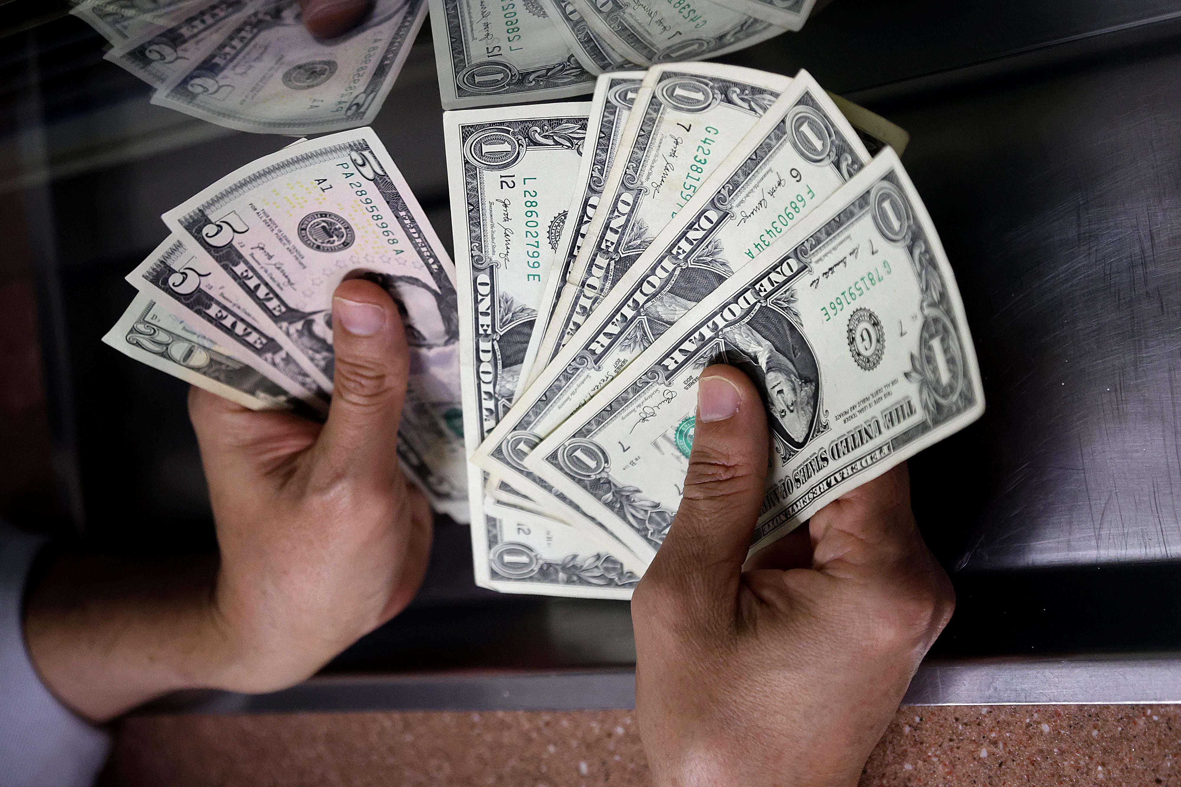 Manos contando billetes de dólares en una ventanilla de cambio, representando la abundancia de divisas que afecta el tipo de cambio en Costa Rica, según un estudio del Banco Central.