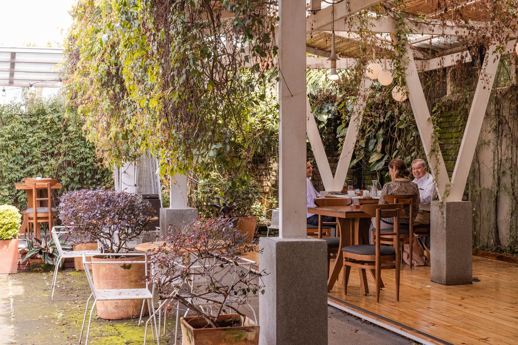 Cafetería Cafeoteca en Barrio Escalante, San José, Costa Rica, con mesas al aire libre y rodeada de vegetación, donde clientes disfrutan de su café. Seleccionada entre las 100 mejores cafeterías del mundo en 2025.