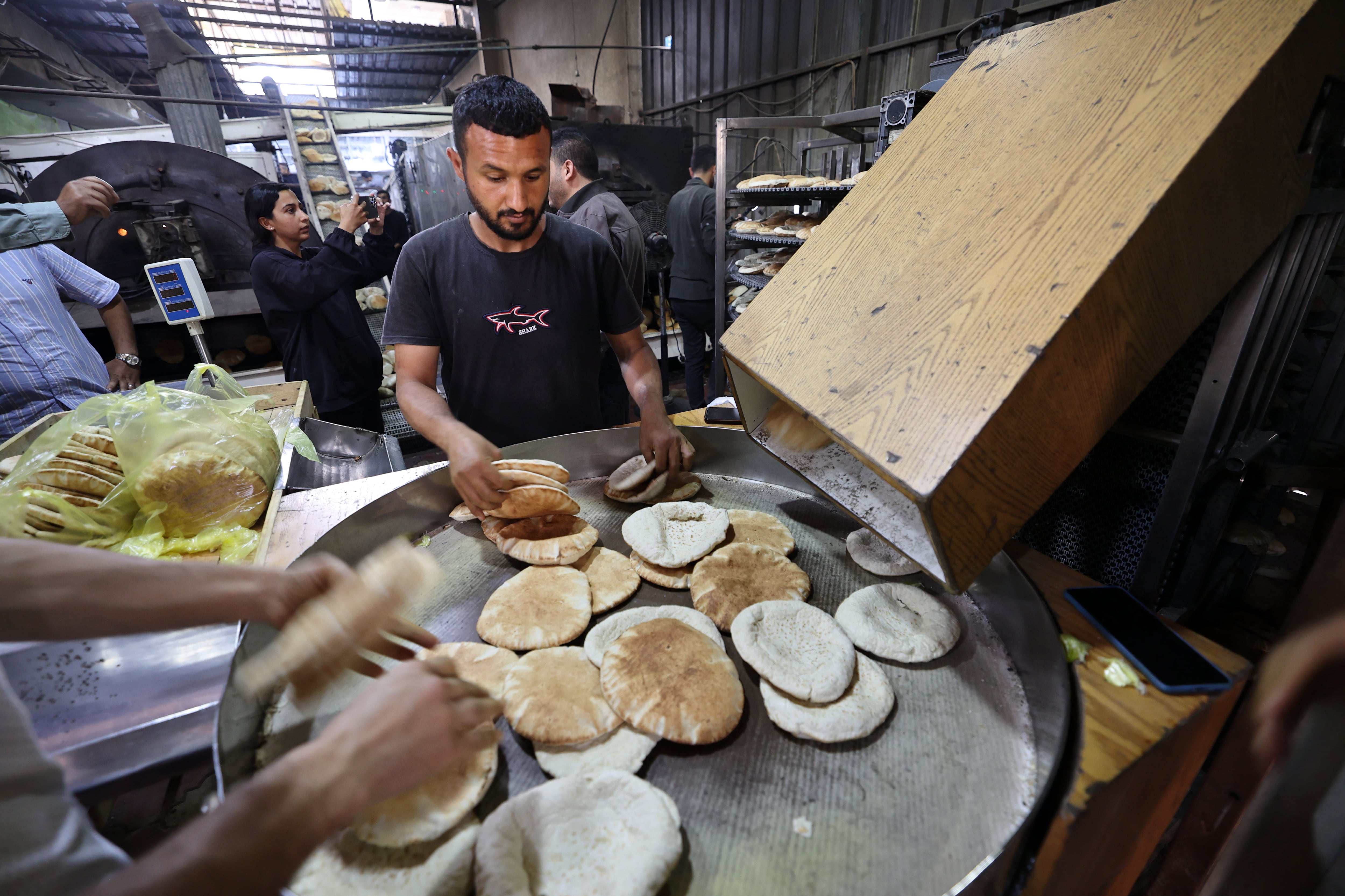 Empleados de una panadería en Deir el-Balah, en el centro de la Franja de Gaza, llenan bolsas con pan recién horneado, después de que Israel permitiera la entrada de ayuda humanitaria limitada al territorio palestino este 22 de mayo. Fotografía: