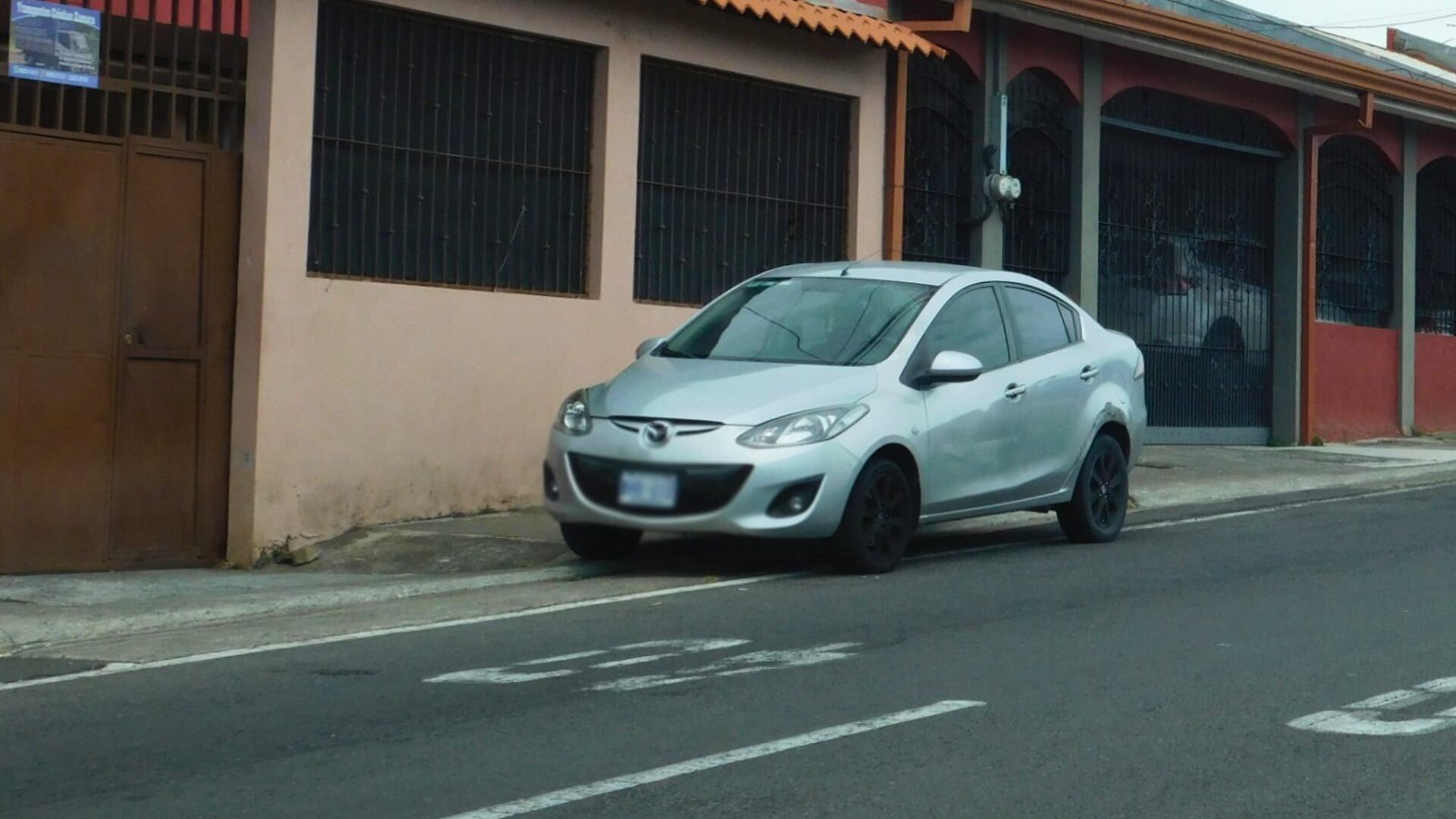 Vehículo tipo sedán color plateado estacionado de forma indebida sobre una acera en un barrio urbano, reflejando una de las infracciones más frecuentes del 2025 según datos del MOPT.