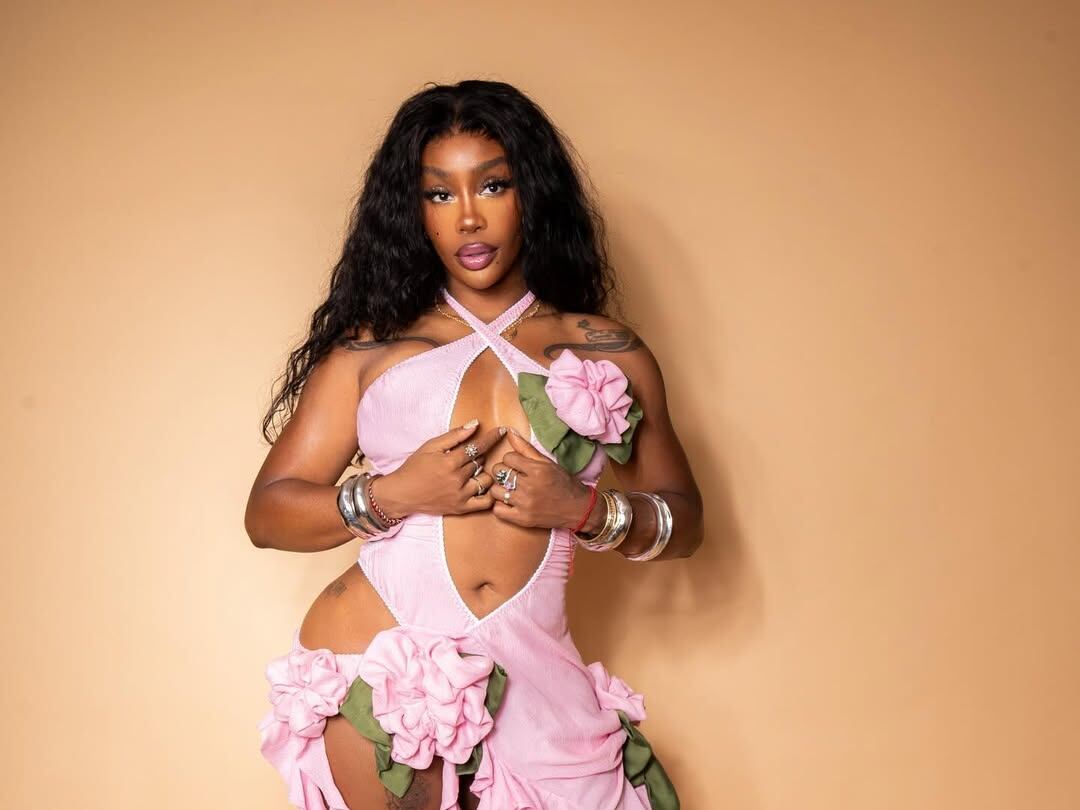 Foto de SZA usando un vestido rosado en un fondo anaranjado.