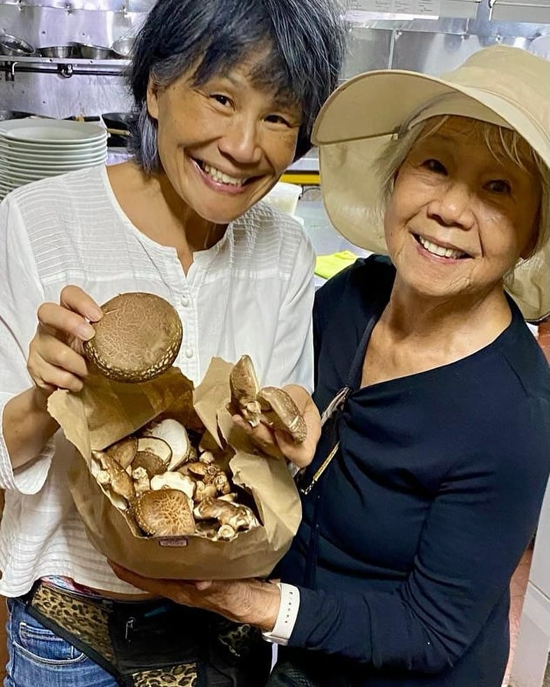 María Hon y su madre Doña Rosa sostienen hongos shitake producidos en San Gerardo de Dota, uno de los proveedores que forman parte de la extensa red de abastecimiento local que el Tin Jo cultivó durante décadas. "Sentimos una profunda gratitud con toda la comunidad Tin Jo", dijo Hon al anunciar su retiro.