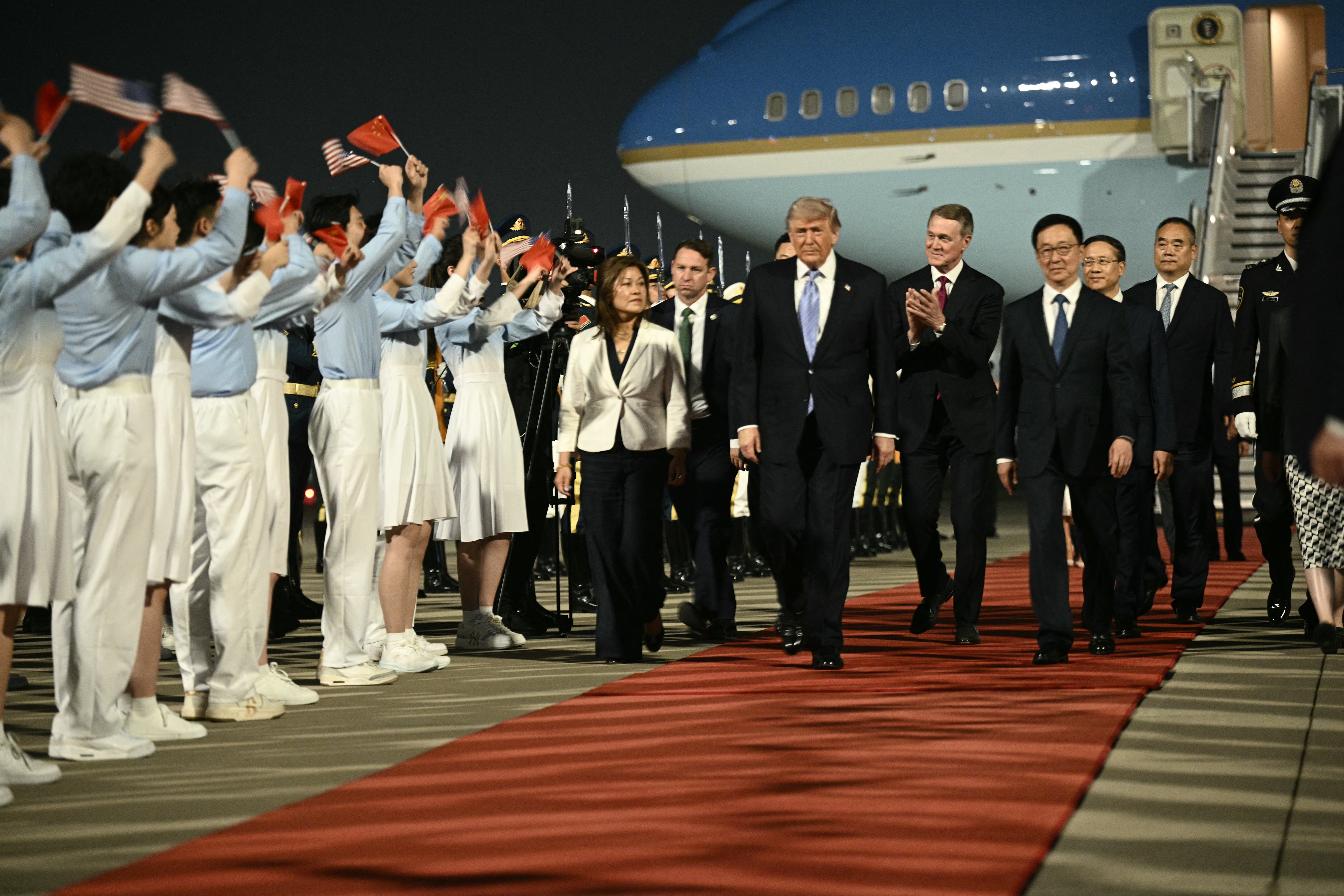 El presidente de Estados Unidos, Donald Trump (centro), y el embajador estadounidense en China, David Perdue (centro derecha), acompañados por el vicepresidente chino, Han Zheng (derecha), recibieron el saludo de jóvenes chinos tras llegar al Aeropuerto Internacional de Pekín este 13 de mayo del 2026. Foto: Brendan Smialowski / AFP.