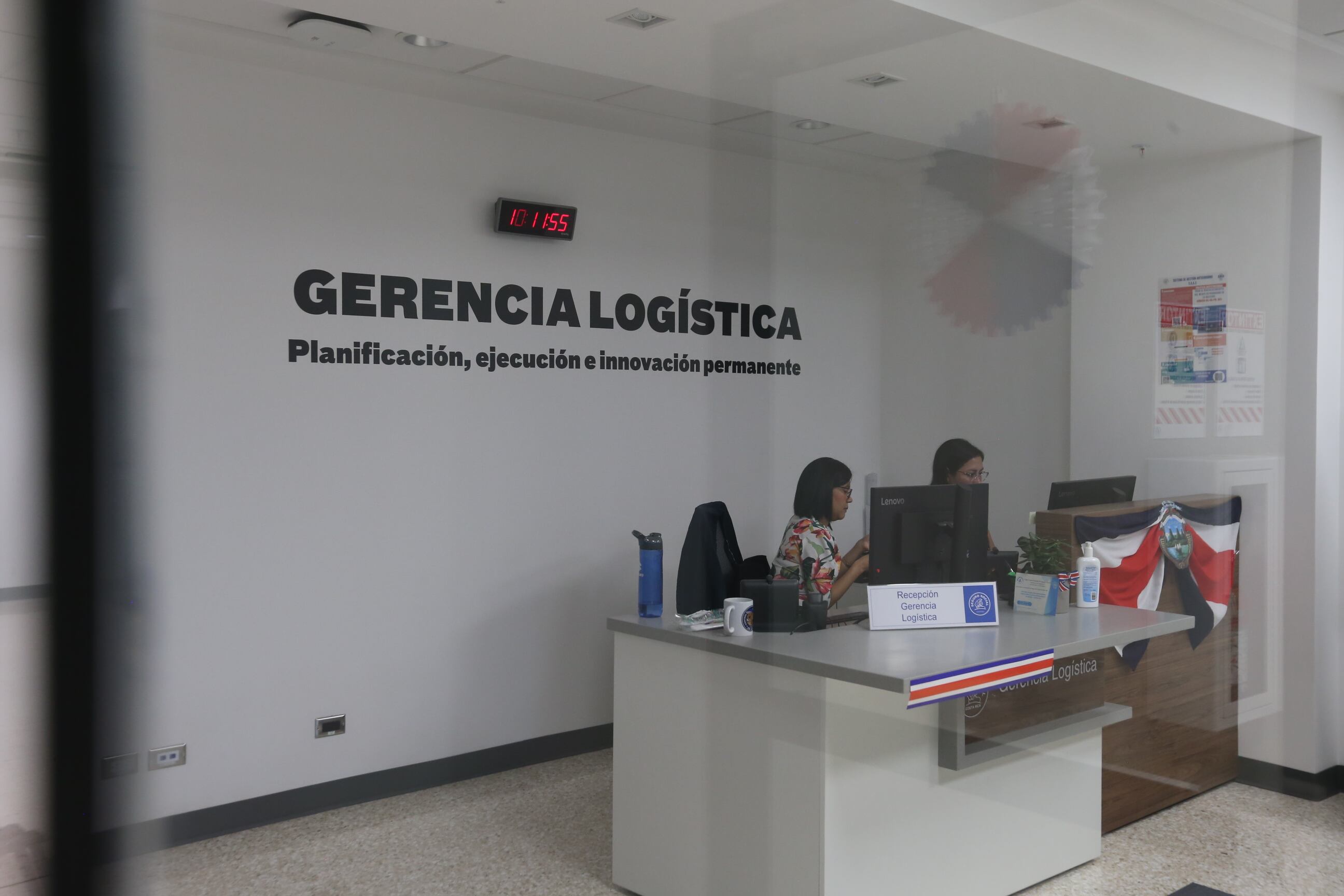 Oficina con paredes blancas y una base de recepción con dos personas.