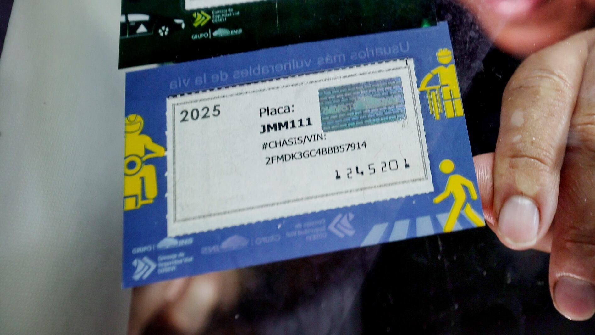 Persona coloca en el parabrisas un marchamo con la placa del vehículo. Hacienda actualizó los tramos del impuesto a la propiedad vehicular, base del marchamo 2026.