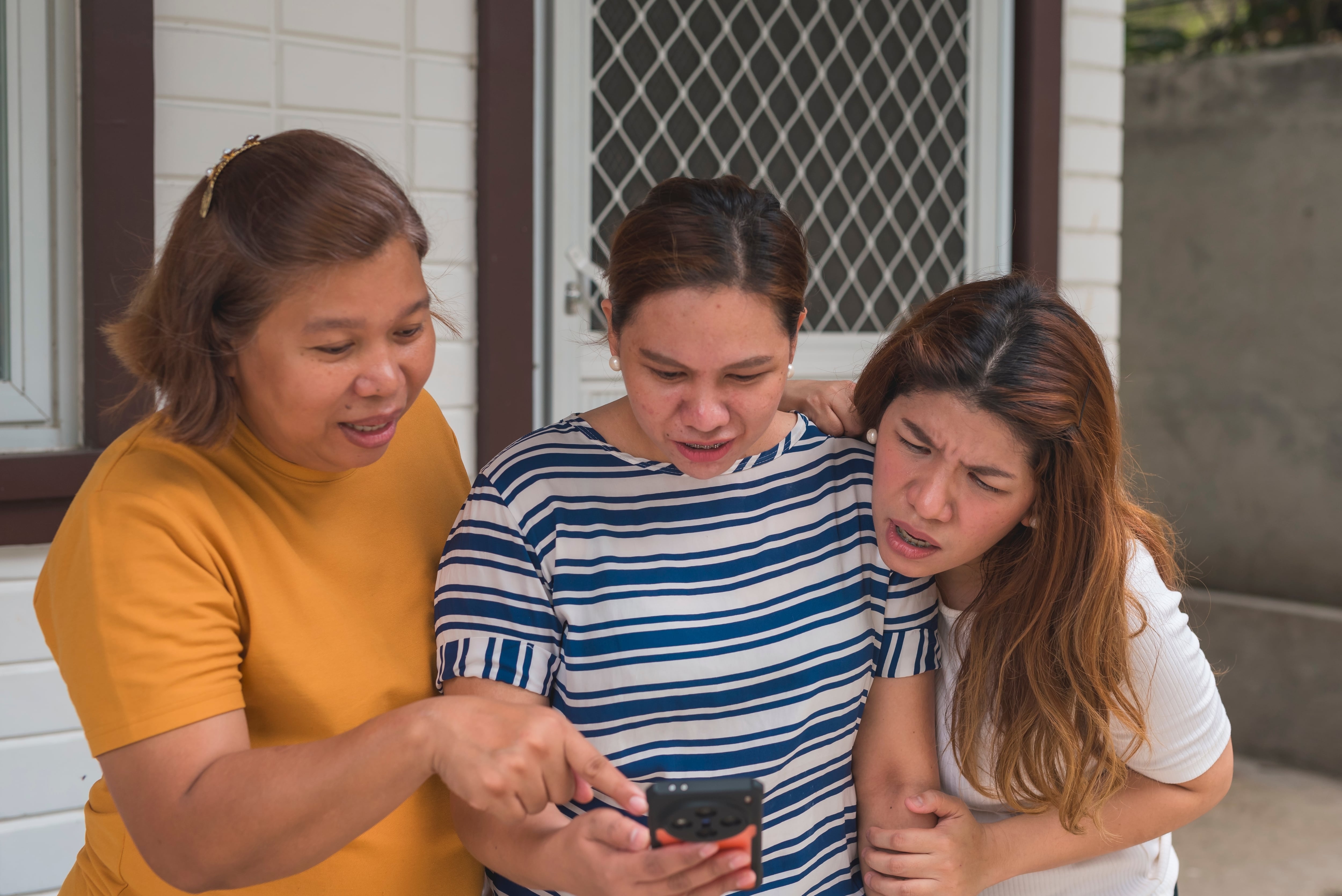 Tres mujeres chismean, vinean, fisgonean mientras ven información de alguien en el teléfono celular de una de ellas