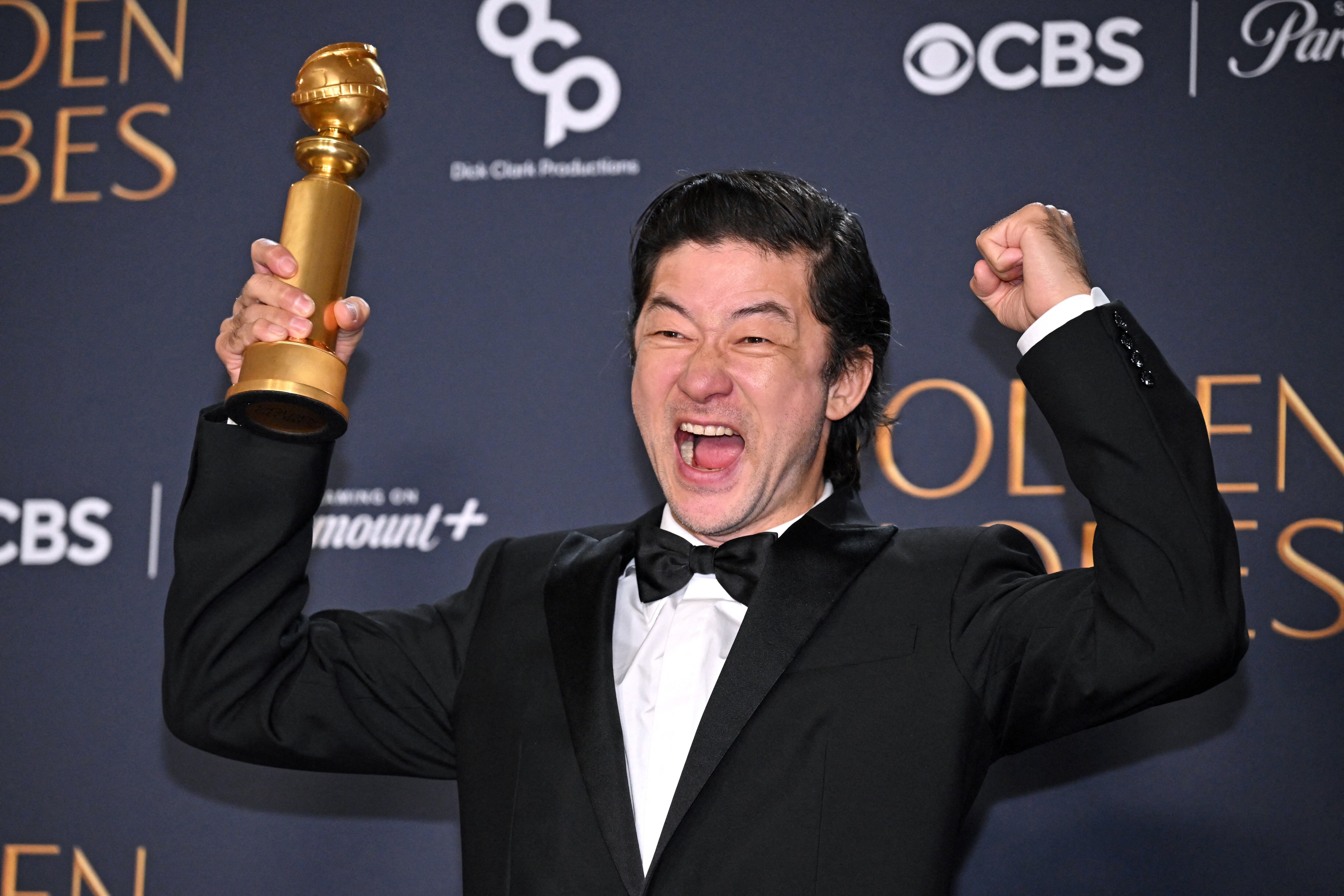 Imagen del actor japonés Tadanobu Asano sosteniendo en su mano derecha su premio Globo de Oro y alzlando los brazos en símbolo de victoria mientras sonríe.