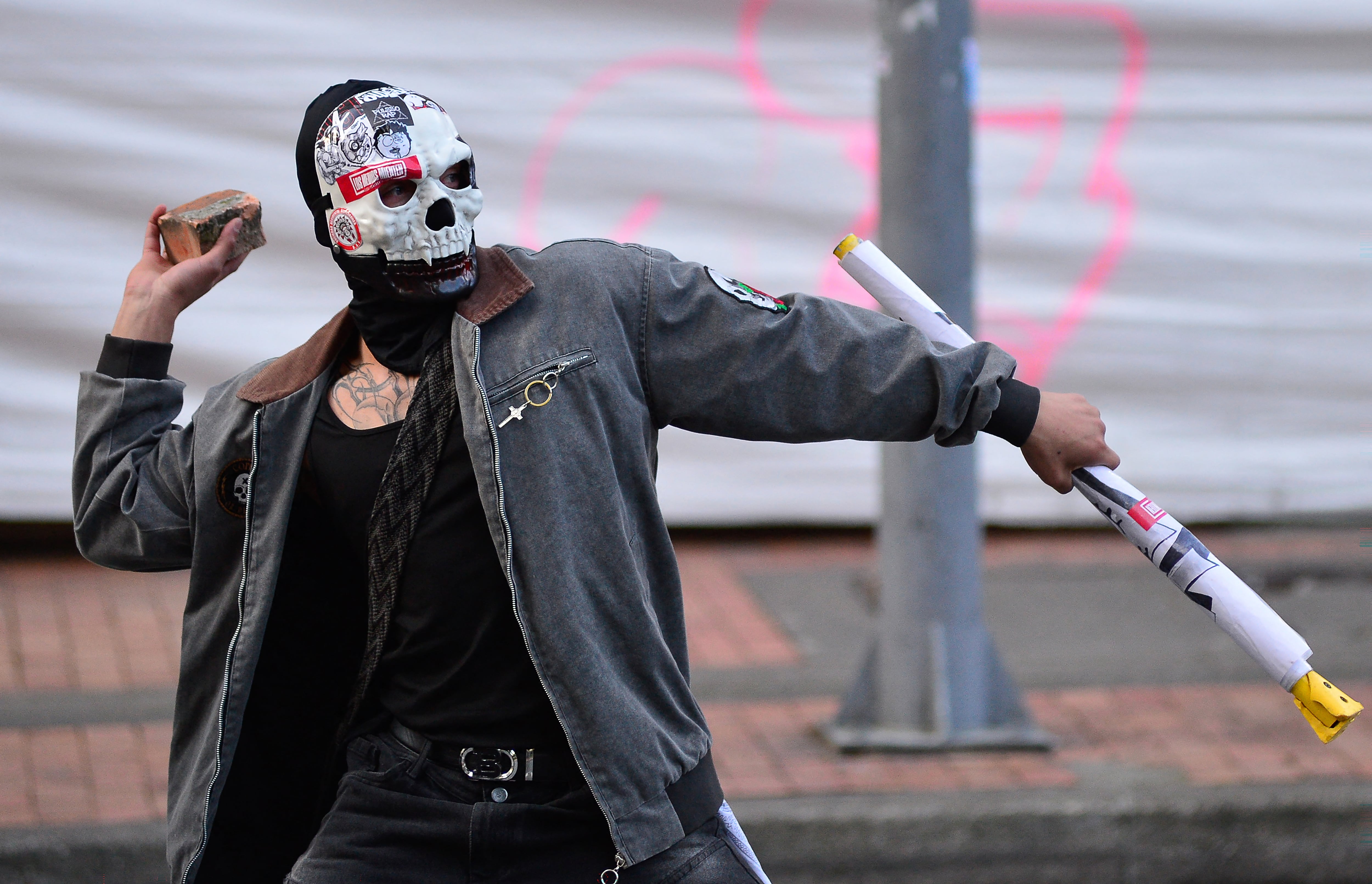 EDITORS NOTE: Graphic content / A demonstrator throws a stone towards police officers during a protest in front of National Museum against a government order to remove works alluding to LGBTQ rights and the country's peace process in Bogota on October 18, 2026. Colombia's new right-wing government has ordered one of the country's top museums to remove dozens of works alluding to LGBTQ rights and the country's peace process, sparking condemnation from visitors. (Photo by Sebastian BARROS / AFP)