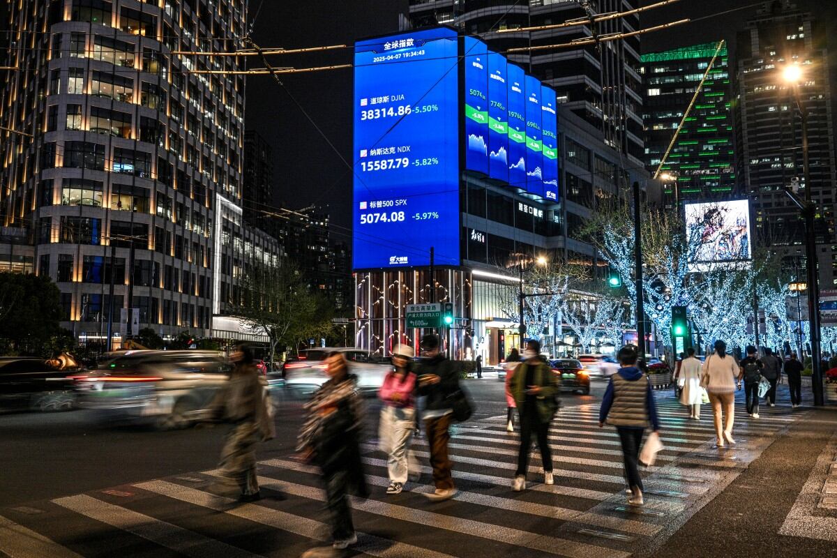 People walk next to a screen with a stocks indicator in the Jing'an district in Shanghai