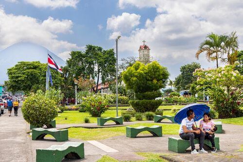 Personas descansando en un parque rodeado de vegetación y con una bandera de Costa Rica visible, en un centro turístico del país.