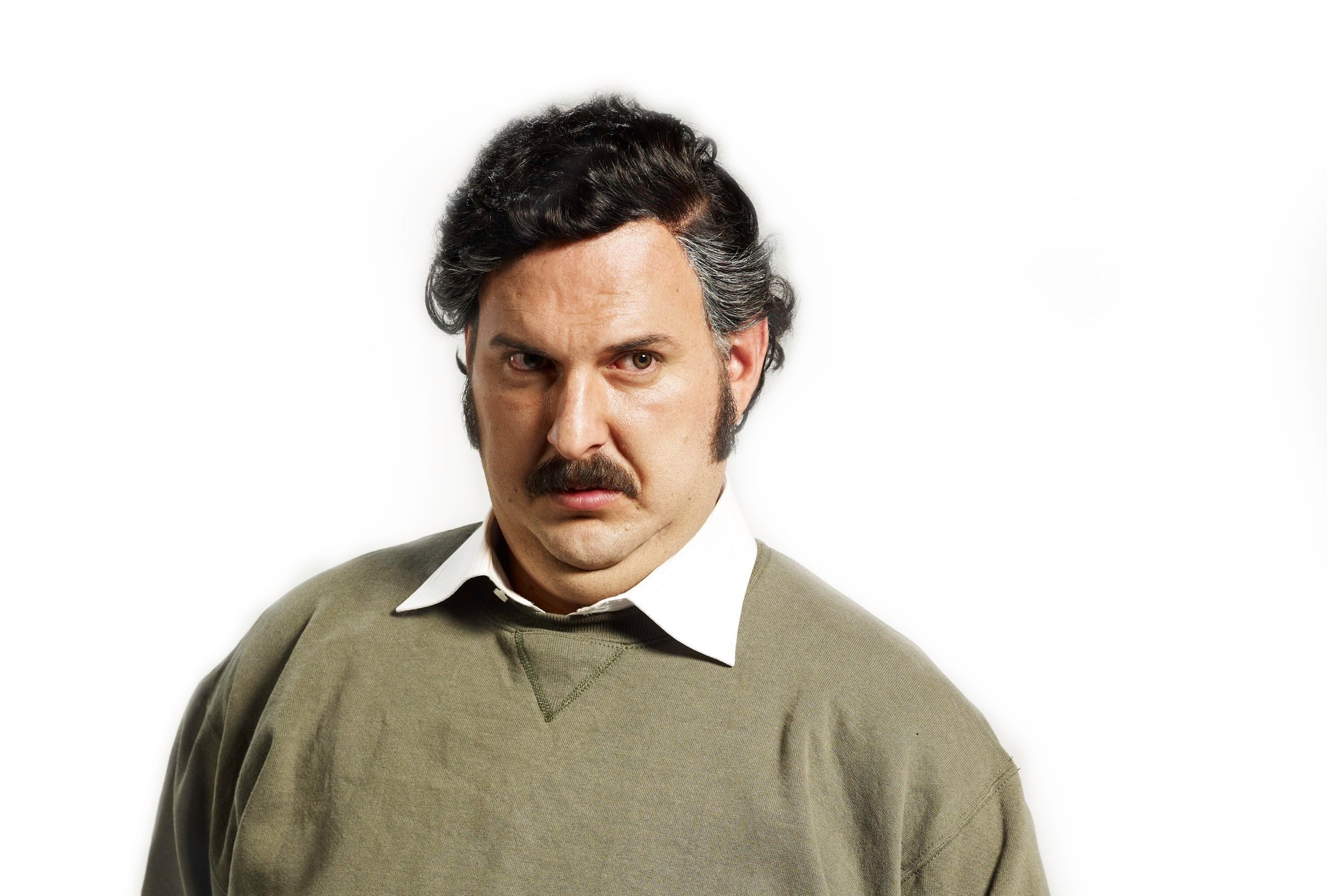 El actor Andrés Parra en su papel de Pablo Escobar, usa bigote, suéter verde y camisa blanca.
