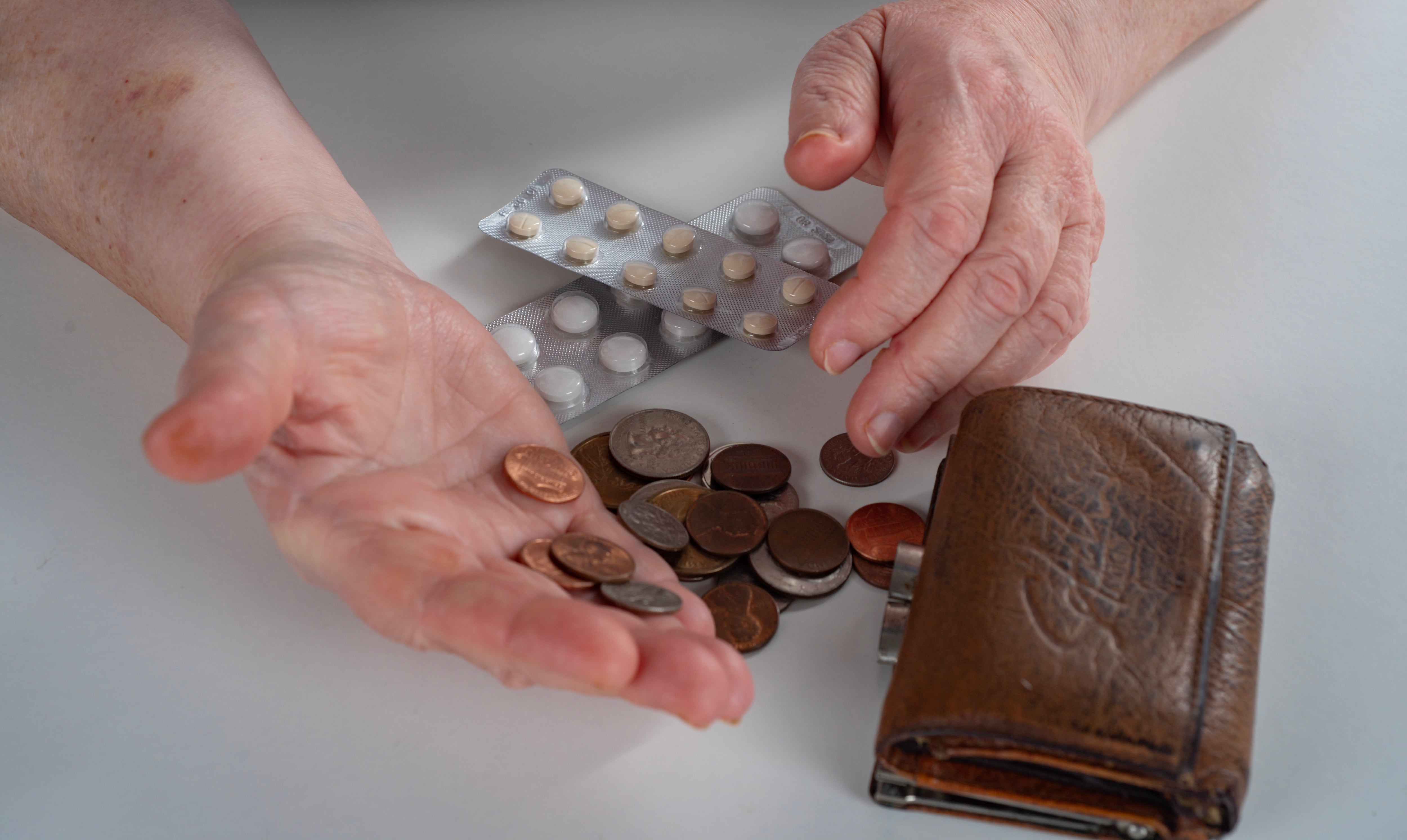 En la imagen unas manos sacando monedas de una billetera para pagar pastillas
