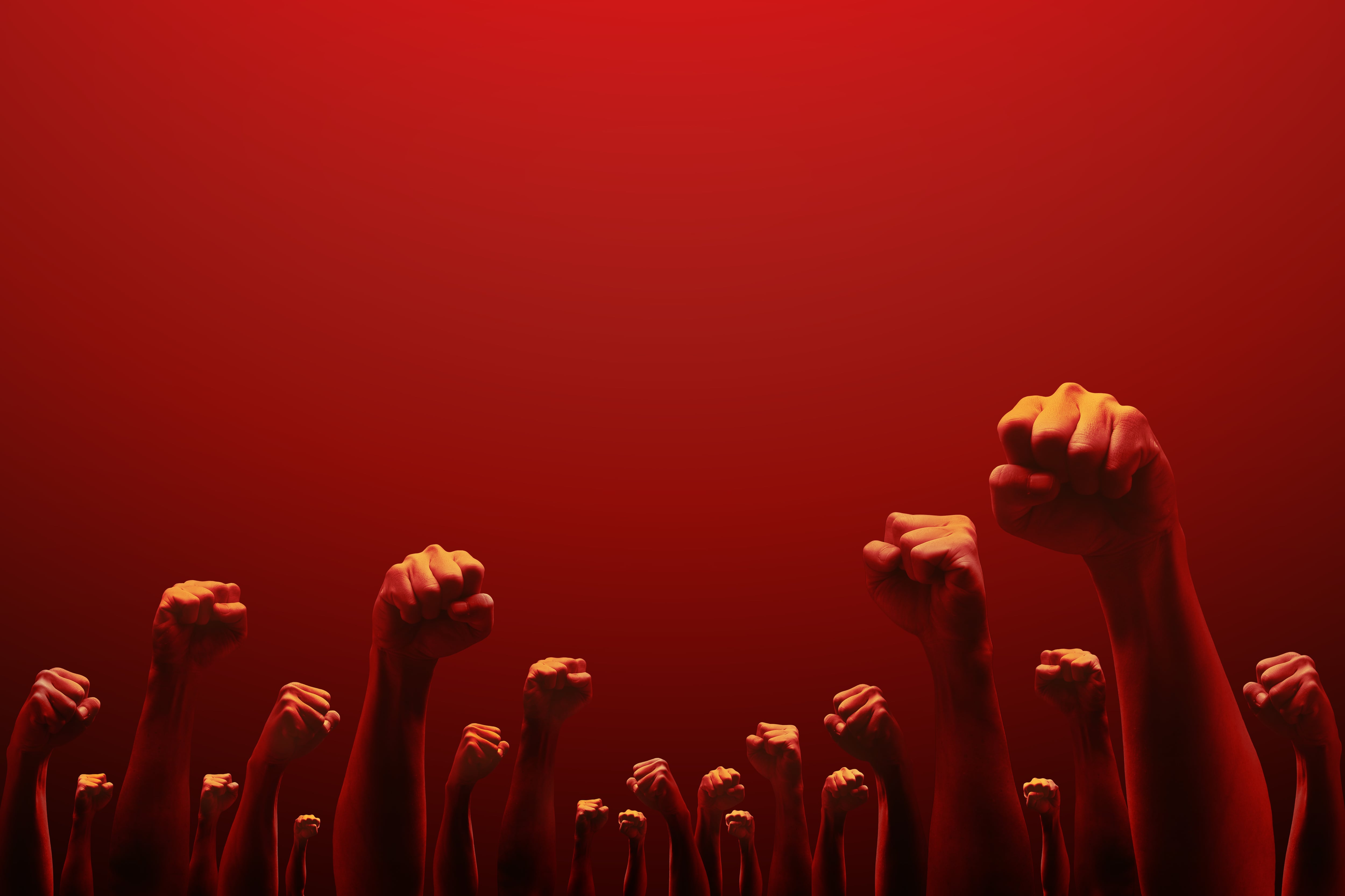 Muchos puños en alto, en señal de pelea, contra fondo rojo. Discursos de odio.