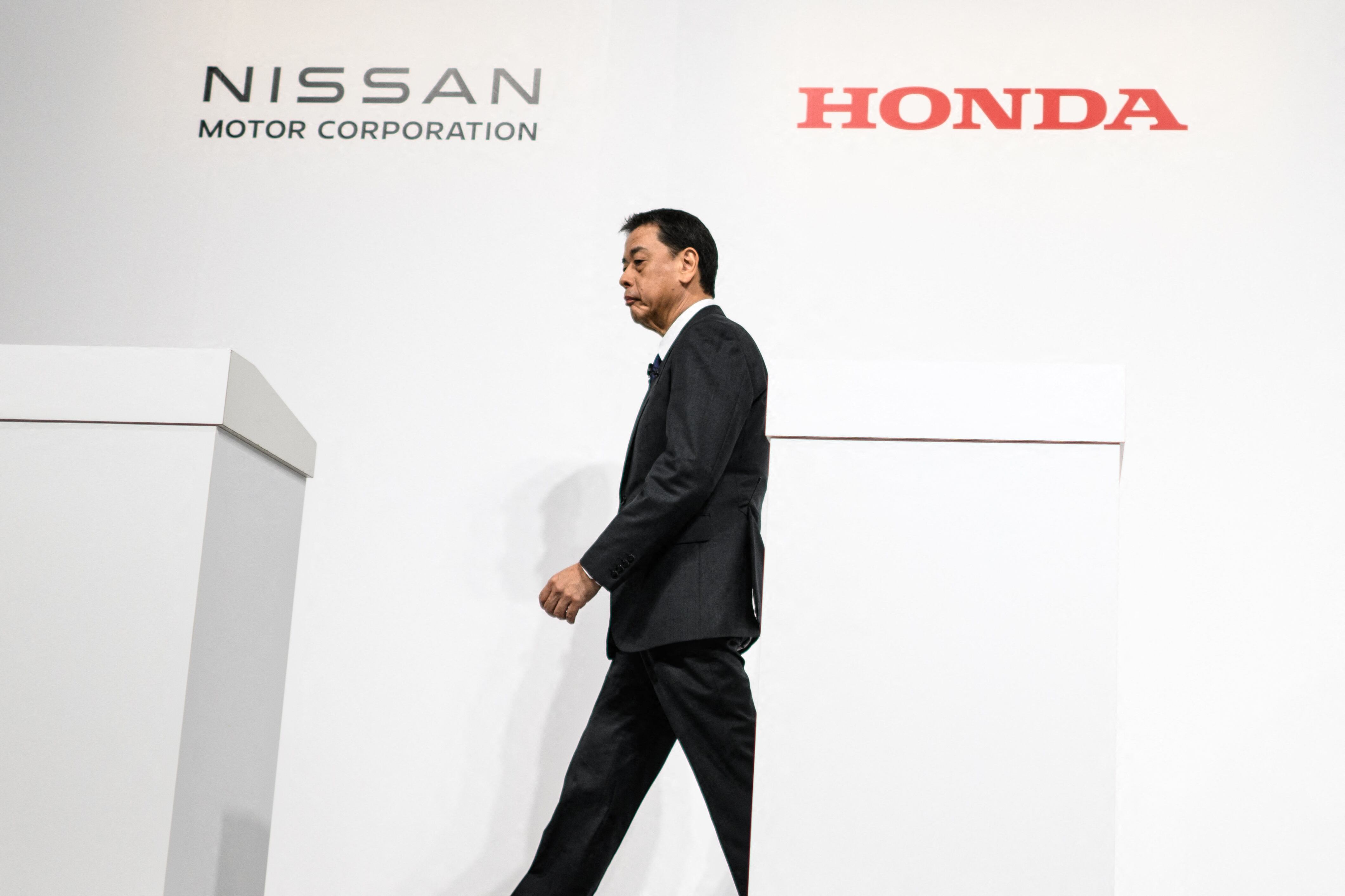 Makoto Uchida, Presidente y CEO de Nissan Motor Corporation, camina frente a los logotipos de Honda y Nissan durante una conferencia de prensa para anunciar una posible fusión de las empresas.