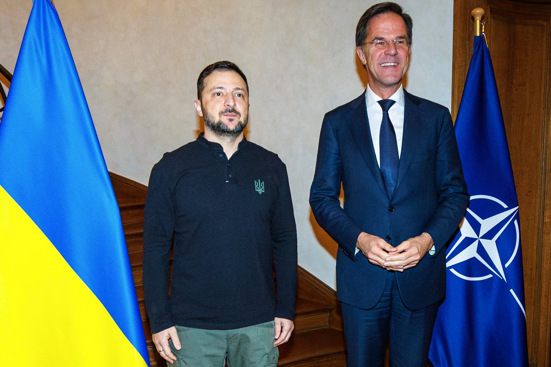 El presidente de Ucrania, Volodymyr Zelensky, y el secretario general de la OTAN, Mark Rutte, de pie junto a las banderas de Ucrania y la OTAN, en una reunión oficial en Bruselas.