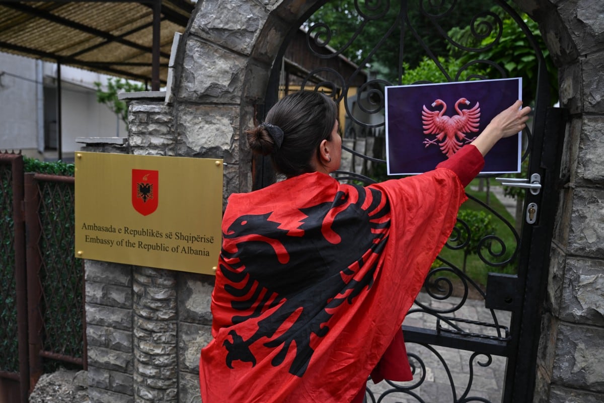 Un manifestante coloca en una puerta un cartel que sustituye el escudo nacional por un águila bicéfala con cabezas de flamenco frente a la Embajada de Albania en Pristina, el 4 de junio de 2026, en una muestra de solidaridad con las protestas que se desarrollan en Albania contra un proyecto turístico de lujo vinculado a Jared Kushner, yerno del presidente estadounidense Donald Trump.