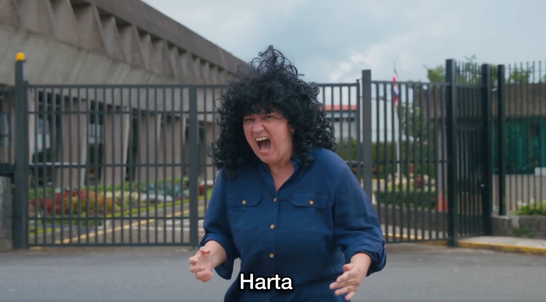 Actriz con peluca negra en una escena de “El chinaoke”, expresando indignación frente a la Casa Presidencial de Costa Rica, en una crítica satírica a problemas sociales.