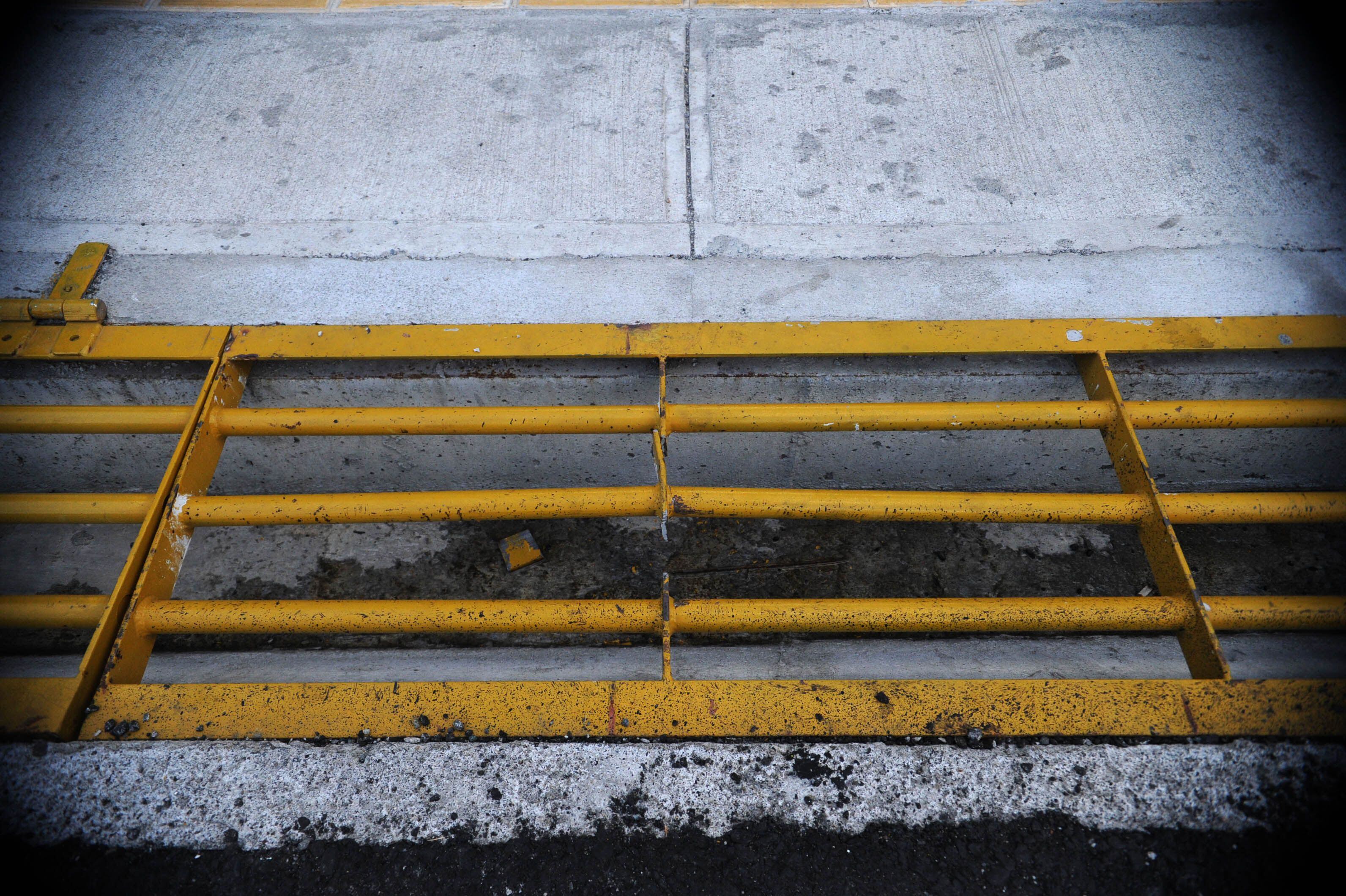 Rejilla metálica amarilla defectuosa en una acera de concreto, que incumple normas de seguridad y puede causar un accidente a un peatón.