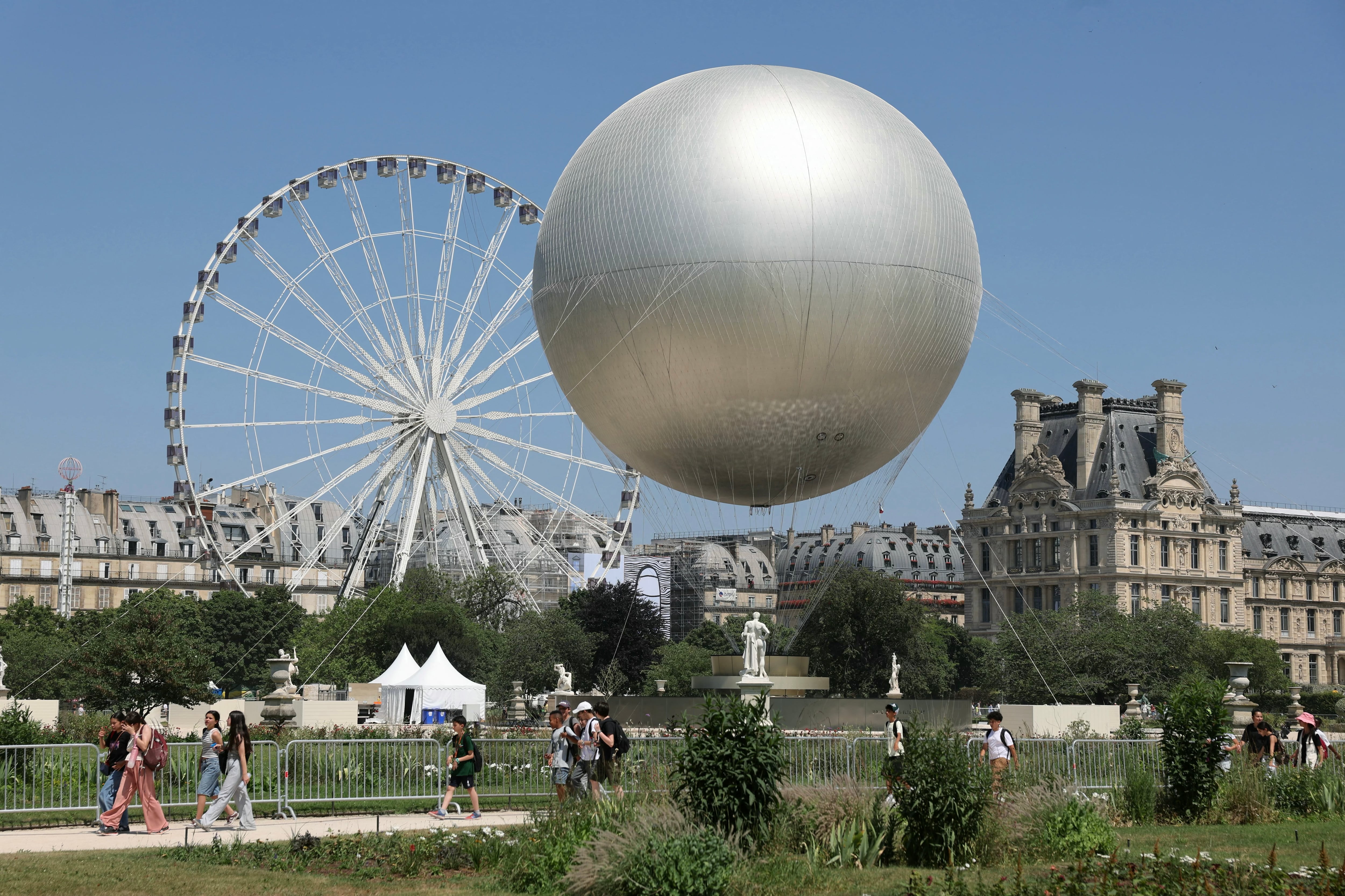 People walk pass by the Olympic Cauldron designed by French designer Mathieu Lehanneur at the Tuileries Garden, during a hot summer afternoon, in Paris, on June 19, 2025. (Photo by Thomas SAMSON / AFP)