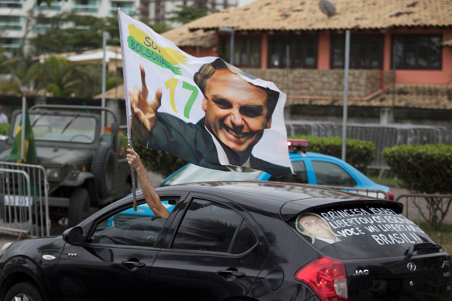 A supporter waves a flag with an image of Jair Bolsonaro as he drives past in front of his residence in Rio de Janeiro, Brazil, Monday, Oct. 29, 2018. Far-right congressman Bolsonaro won Brazil's presidency Sunday on promises to overhaul several aspects of Latin America's largest nation. (AP Photo/Leo Correa)