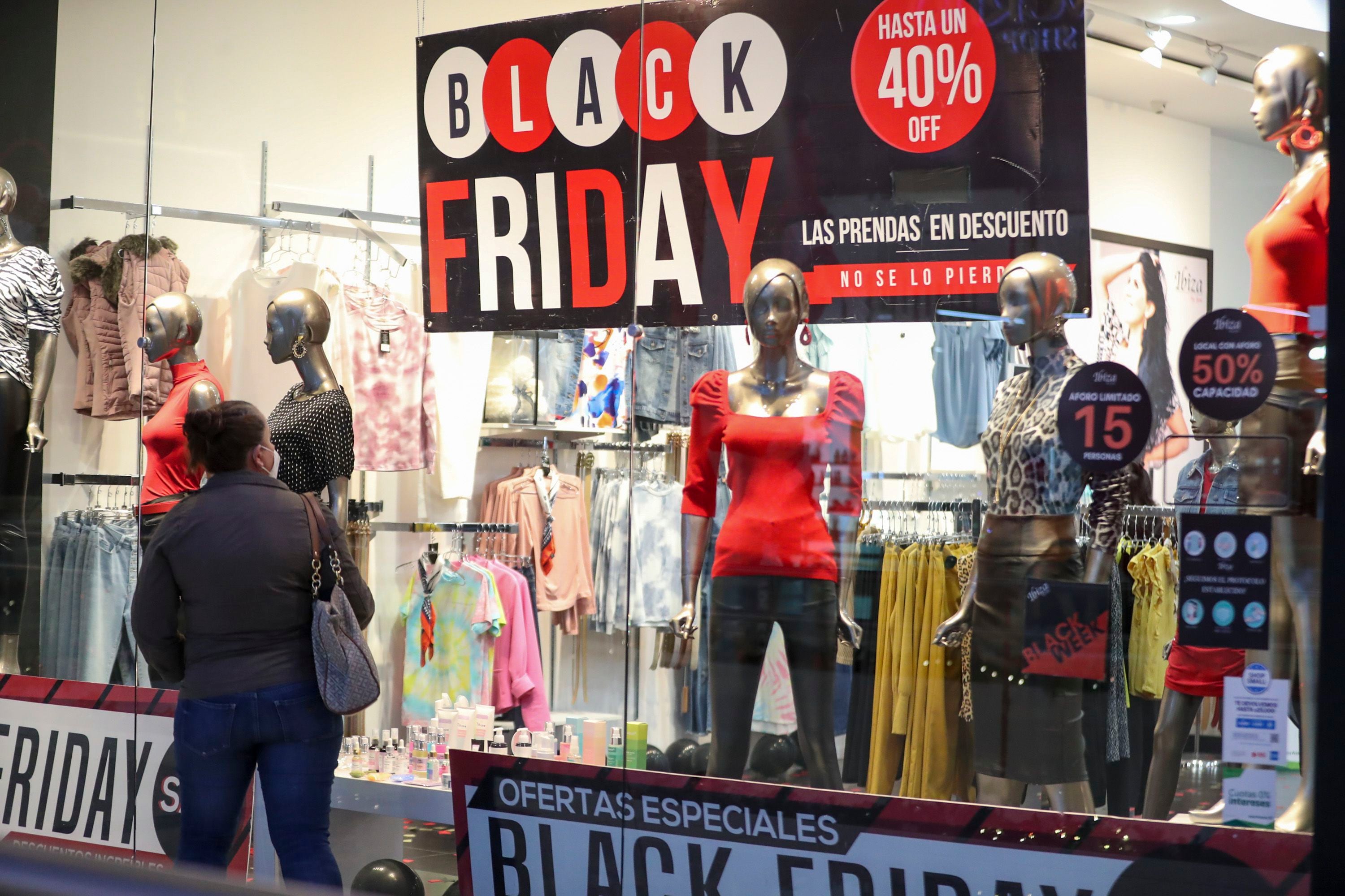 Mujer frente a un escaparate de tienda con maniquíes y un cartel que anuncia descuentos de Black Friday, con ofertas de hasta un 40% de descuento.