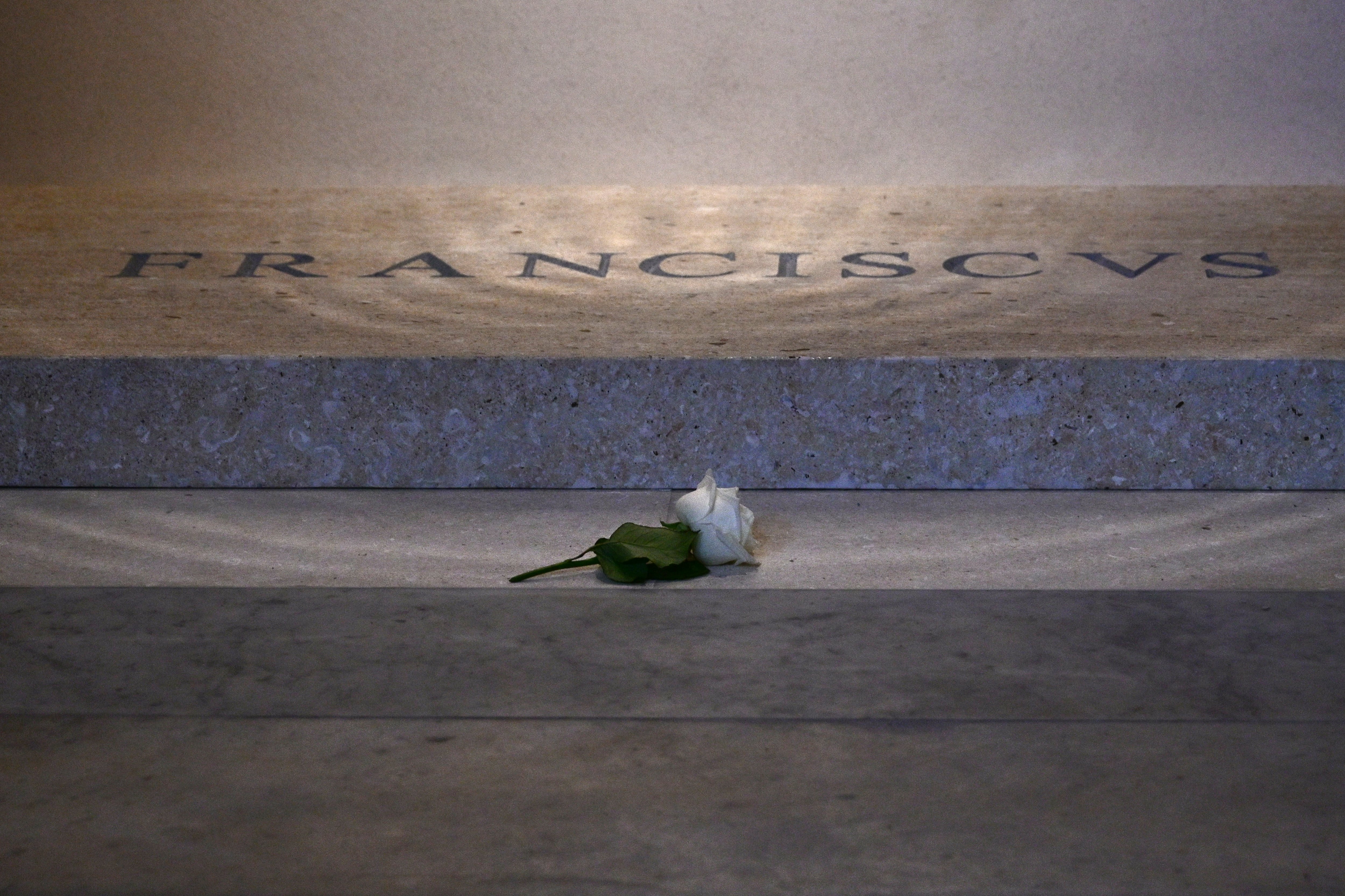 Una imagen en primer plano de la tumba del papa Francisco con sus letras. Tiene una rosa blanca debajo de la placa.