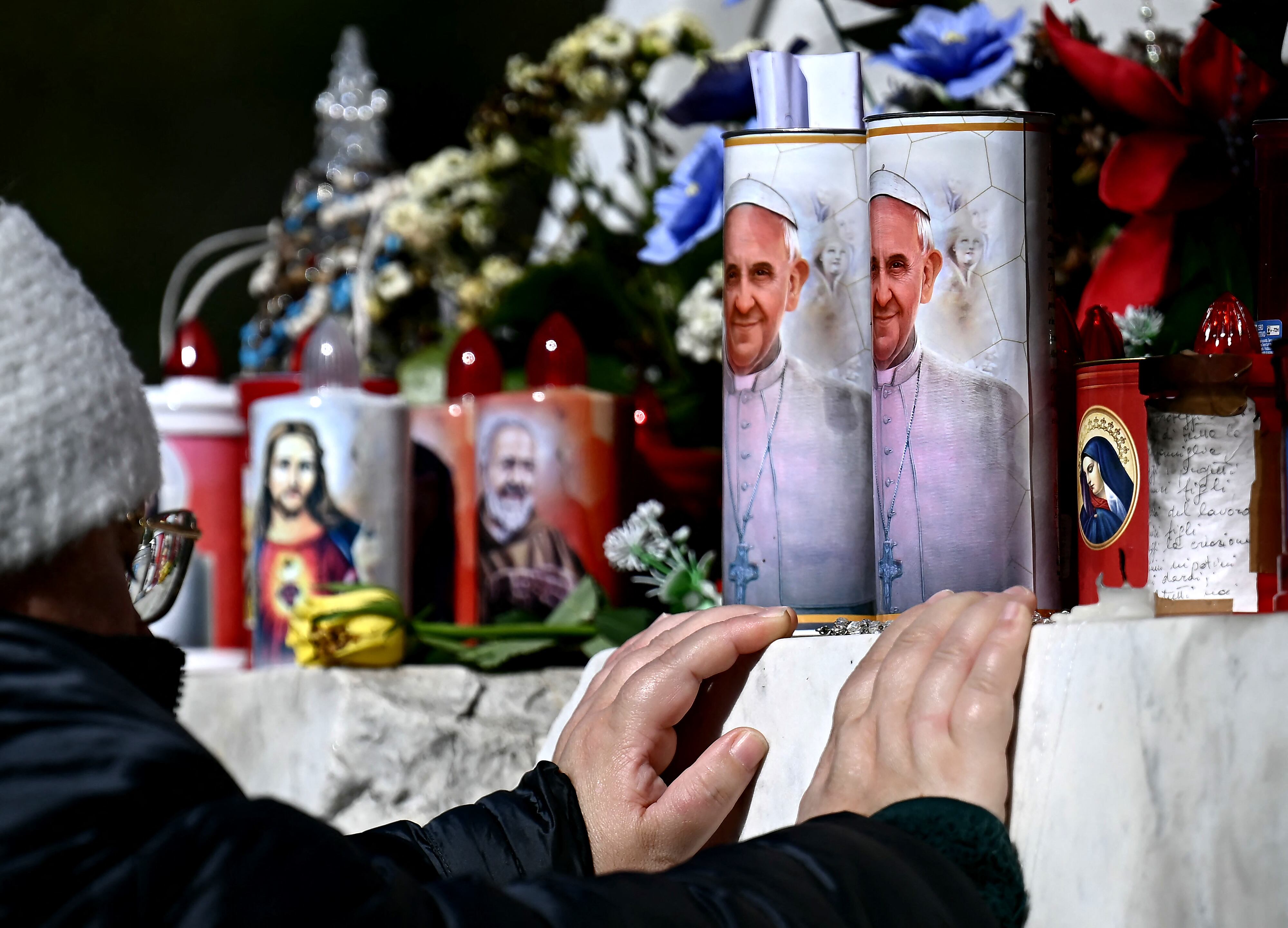 A woman prays in front of candles with a portrait of Pope Francis outside the Gemelli hospital where Pope Francis is hospitalized for tests and treatment for bronchitis in Rome, on February 21, 2025. Pope Francis passes another calm night in hospital, the Vatican said on February 21, 2025 in its morning update, as the 88-year-old spent his seventh day in hospital being treated for pneumonia. (Photo by FILIPPO MONTEFORTE / AFP)