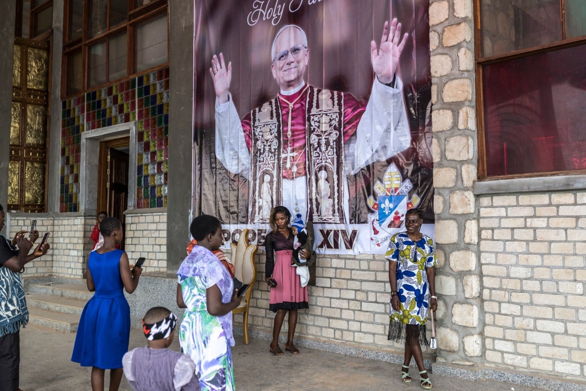 Fieles católicos posan para una foto junto a un cartel que da la bienvenida al papa León XIV, antes de su visita, tras la misa dominical en la catedral metropolitana de San José en Bamenda, el 12 de abril de 2026.