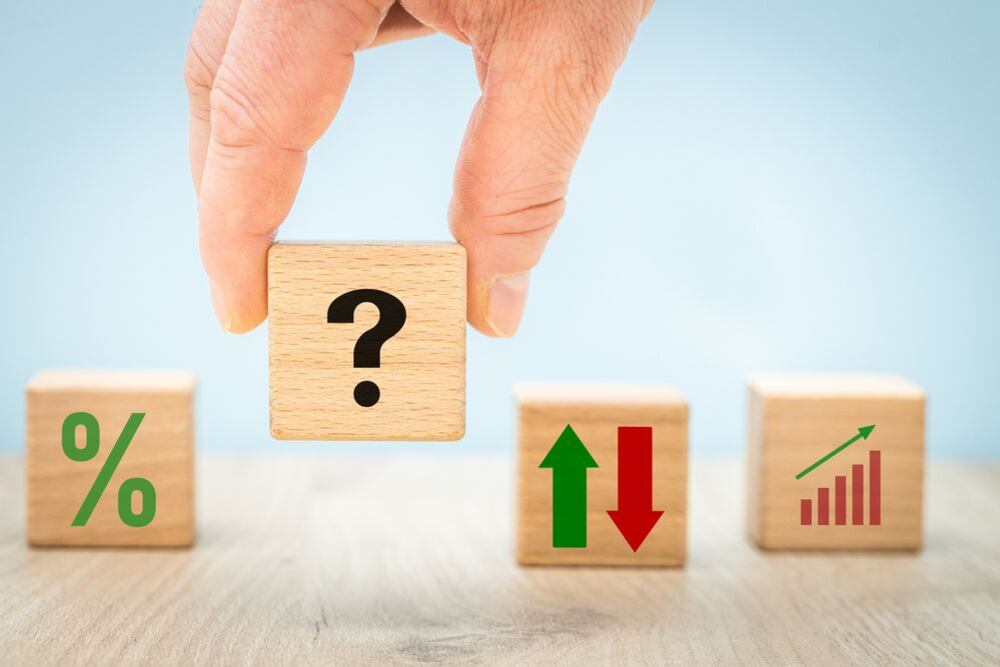 Mano sosteniendo un cubo con signo de interrogación, junto a bloques con símbolos de tasas de interés y tendencias económicas, ilustrando la incertidumbre sobre la TPM en Costa Rica tras el informe de Fitch Ratings.