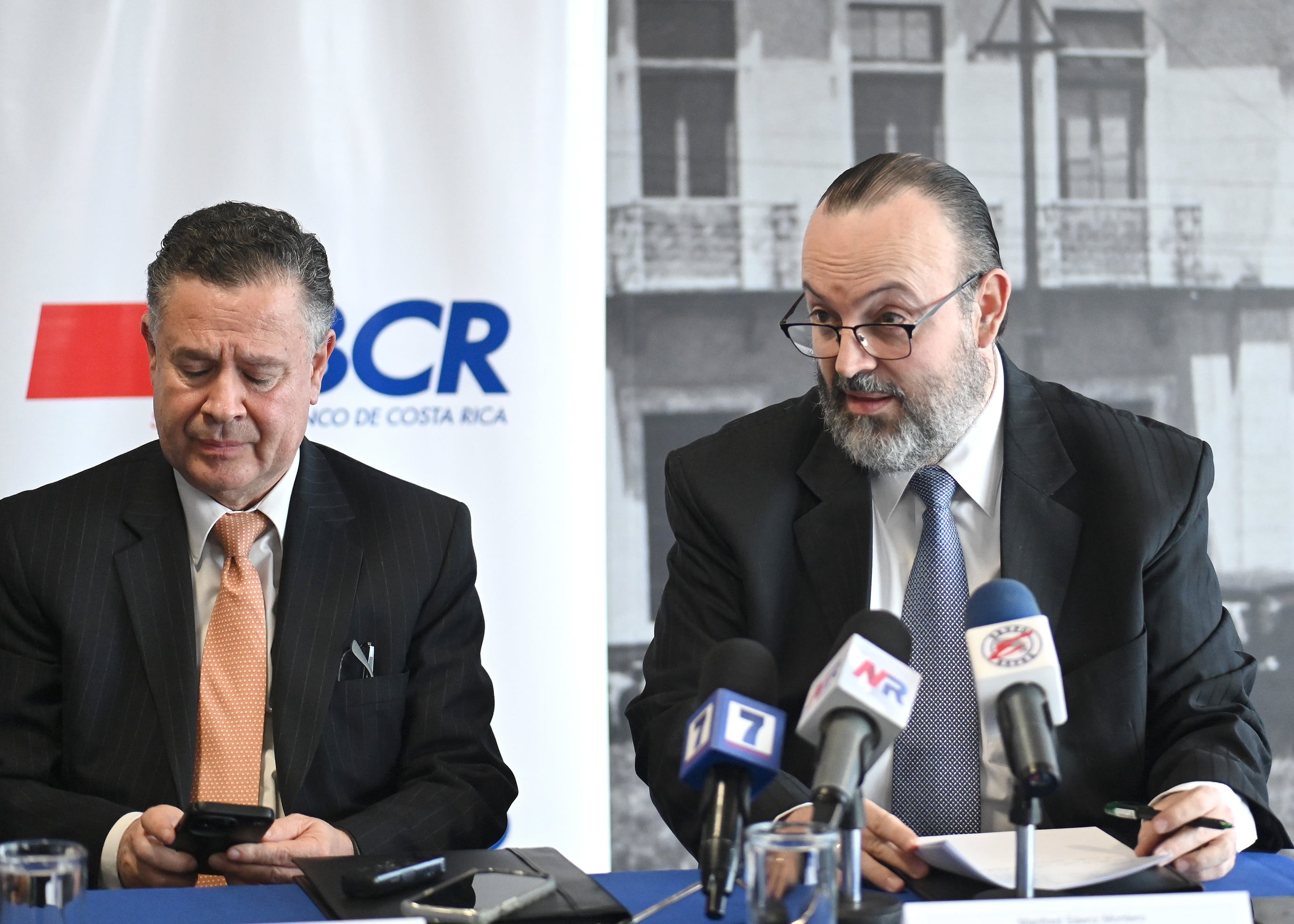 Douglas Soto, gerente general del BCR, y Manfred Sáenz, gerente corporativo jurídico, sentados hablan en una conferencia de prensa.