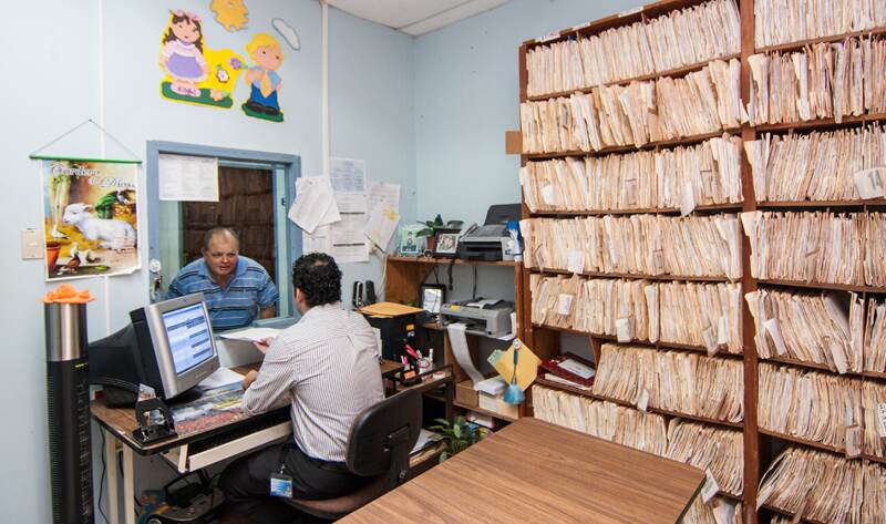 Fabián Anchía (de espaldas) atendió a Víctor Segura en un Ebáis de Puriscal. Aquí, los expedientes de papel aún conviven con los sistemas que se están desarrollando para el futuro expediente electrónico. | JEFFREY ZAMORA PARA LN