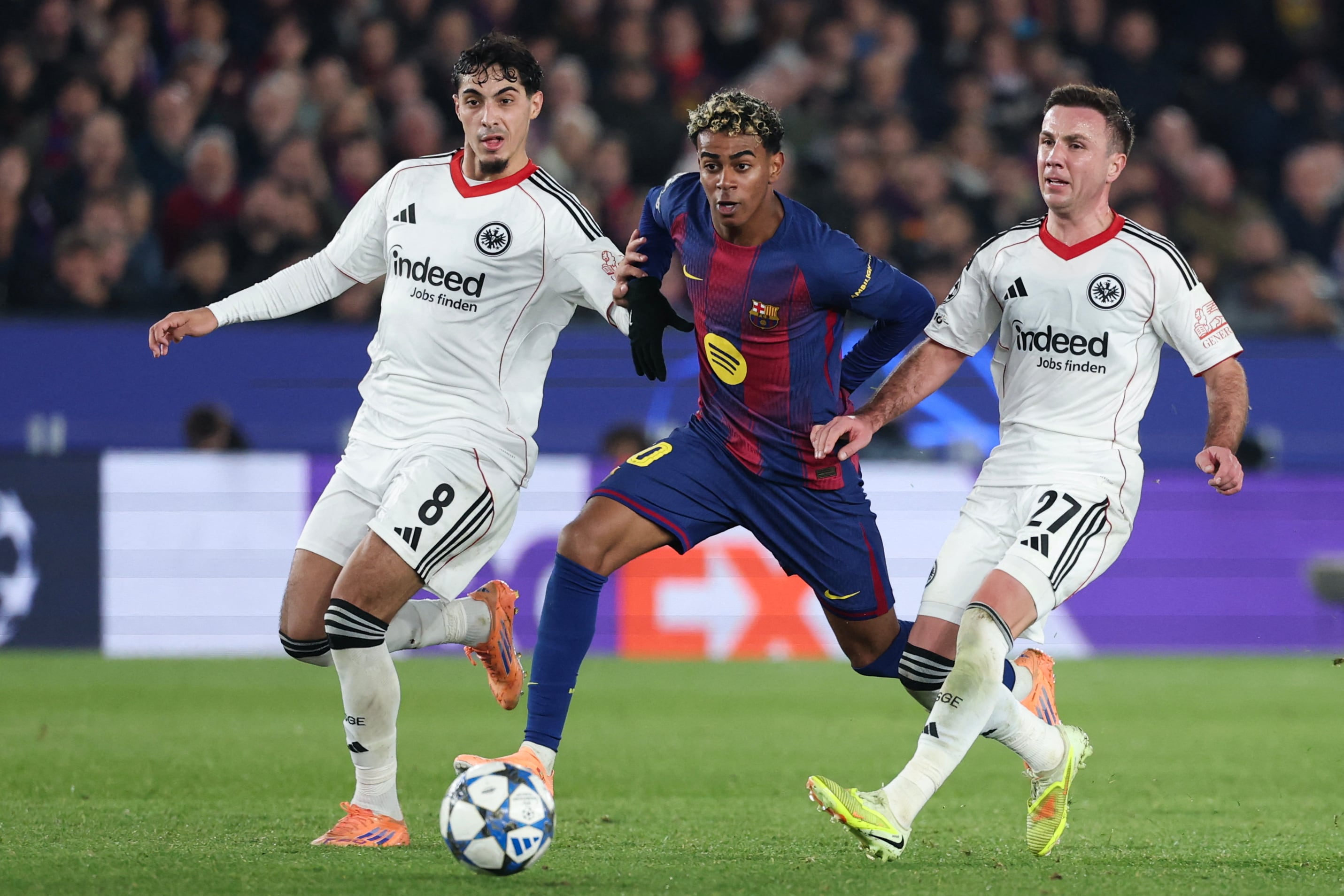 El delantero de Barcelona Lamine Yamal pasa en medio de Fares Chaibi y Mario Goetze, del Eintracht Fráncfort, durante el partido en el Camp Nou por la Champions.